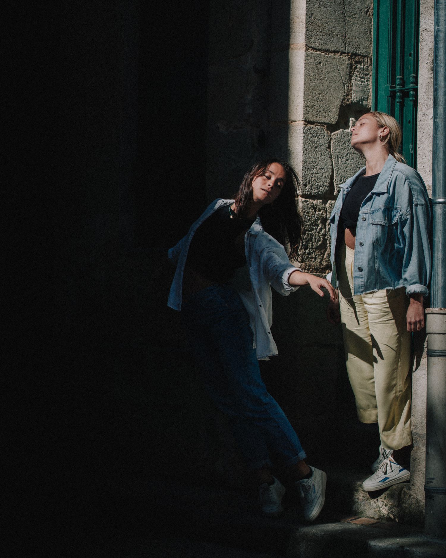 Duo dansant dans une ruelle ombragée, lumière rasante, photo de danse urbaine avec ambiance dramatique.