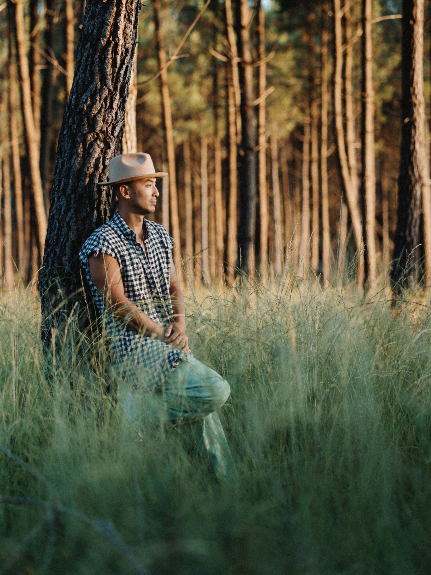 Autoportrait pris dans une clairière de pins, lumière naturelle, assis dans l’herbe, photo personnelle et contemplative.