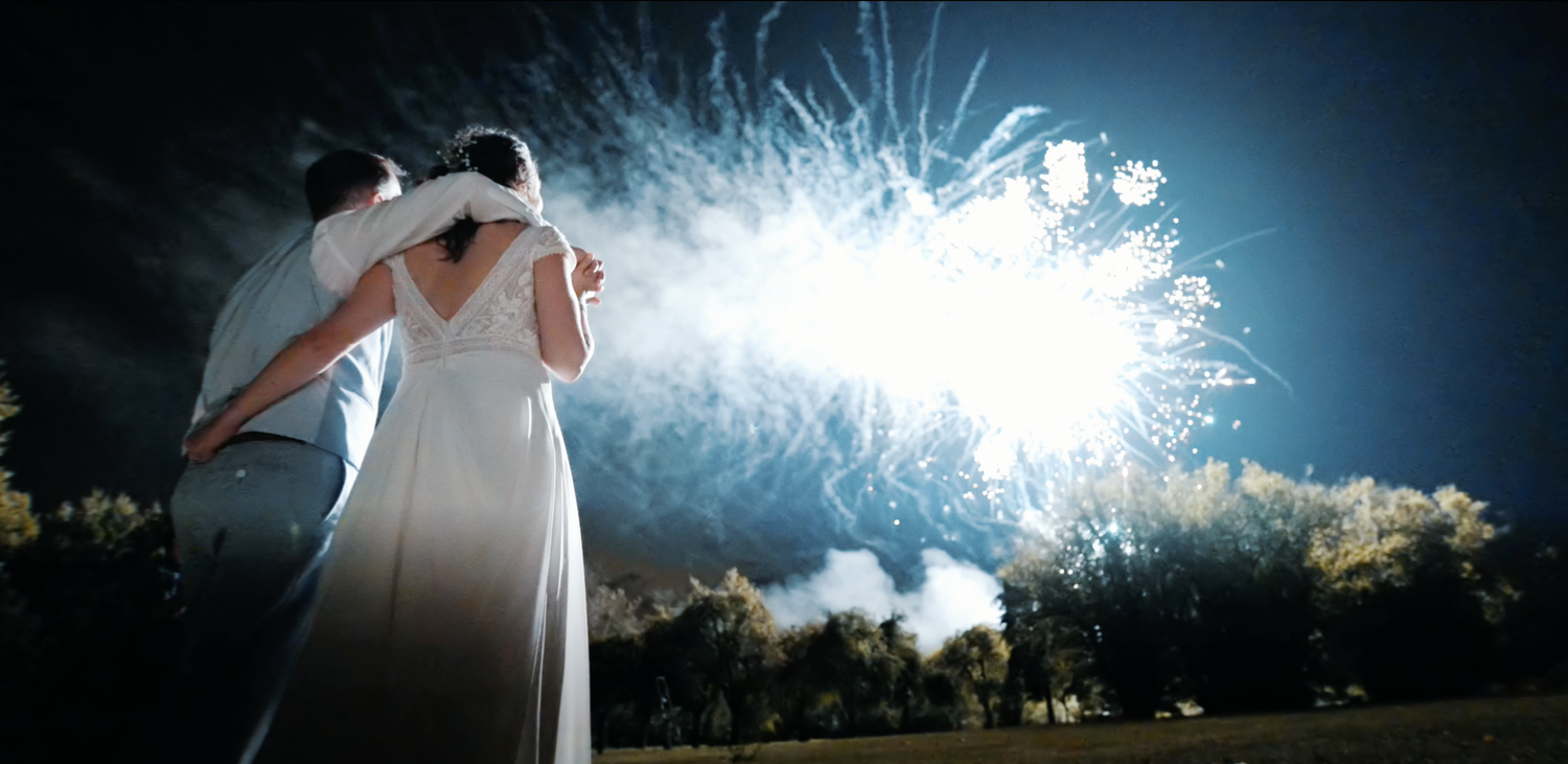 Photo de couple de mariés s’embrassant sous des feux d’artifice, ambiance émotion et célébration nocturne.