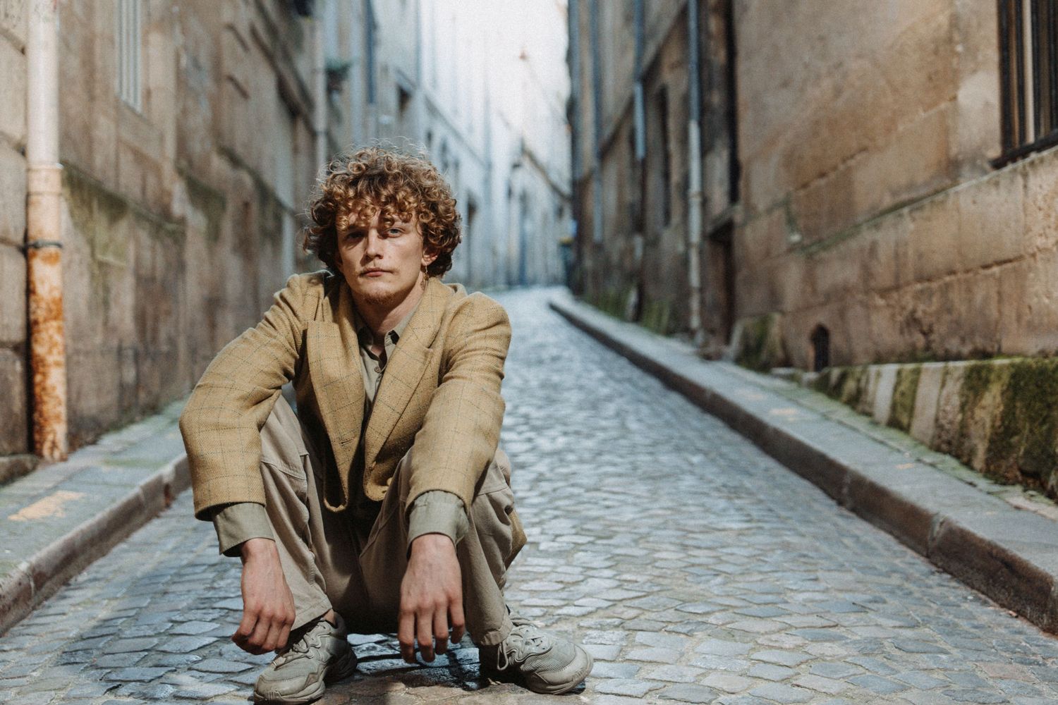 Portrait artistique d’un homme assis sur une rue pavée, ambiance urbaine et naturelle.