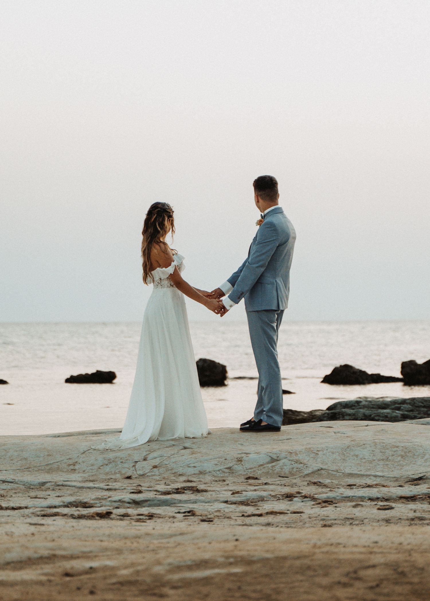 Couple en tenue de mariage sur la plage, ambiance douce au lever du jour, intimité et élégance.
