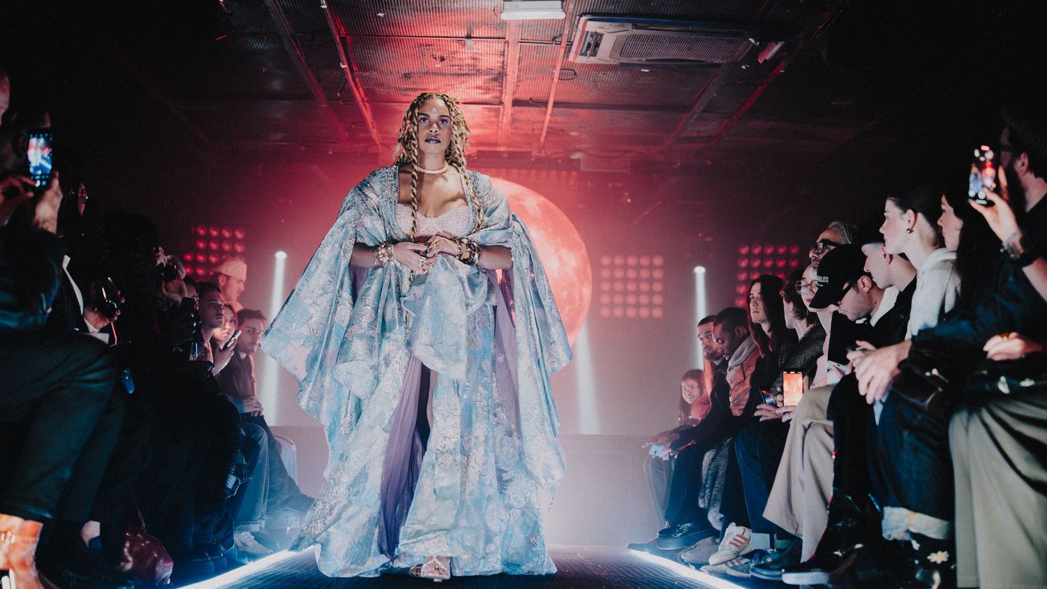 Photo d’un mannequin en tenue haute couture au centre d’un défilé, lumière de scène, ambiance show immersif.