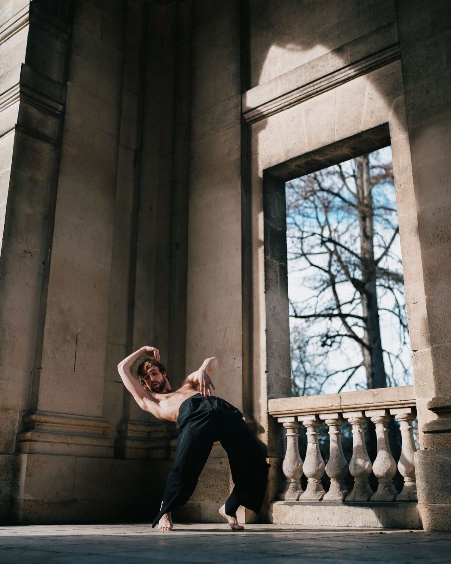 Danse contemporaine dans un lieu patrimonial en pierre, lumière naturelle cadrée, gestuelle fluide et posée.