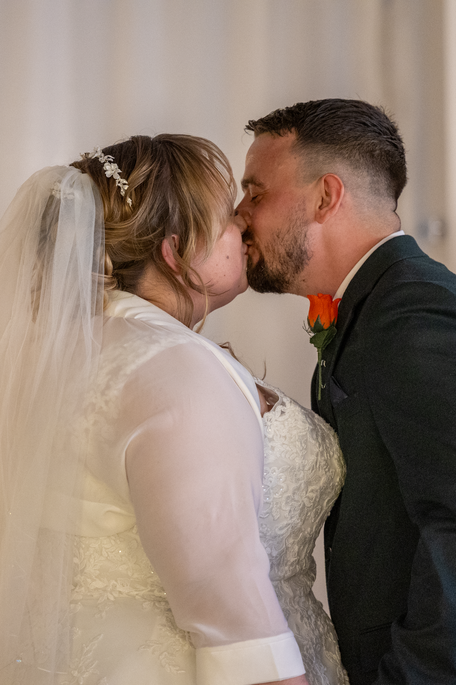 A bride and groom share their first kiss at the wedding altar, bride wearing lace gown and veil, groom in dark suit.