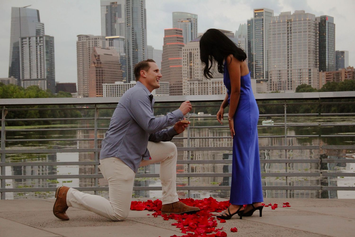 Romantic marriage proposal with red rose petals and urban skyline in background.