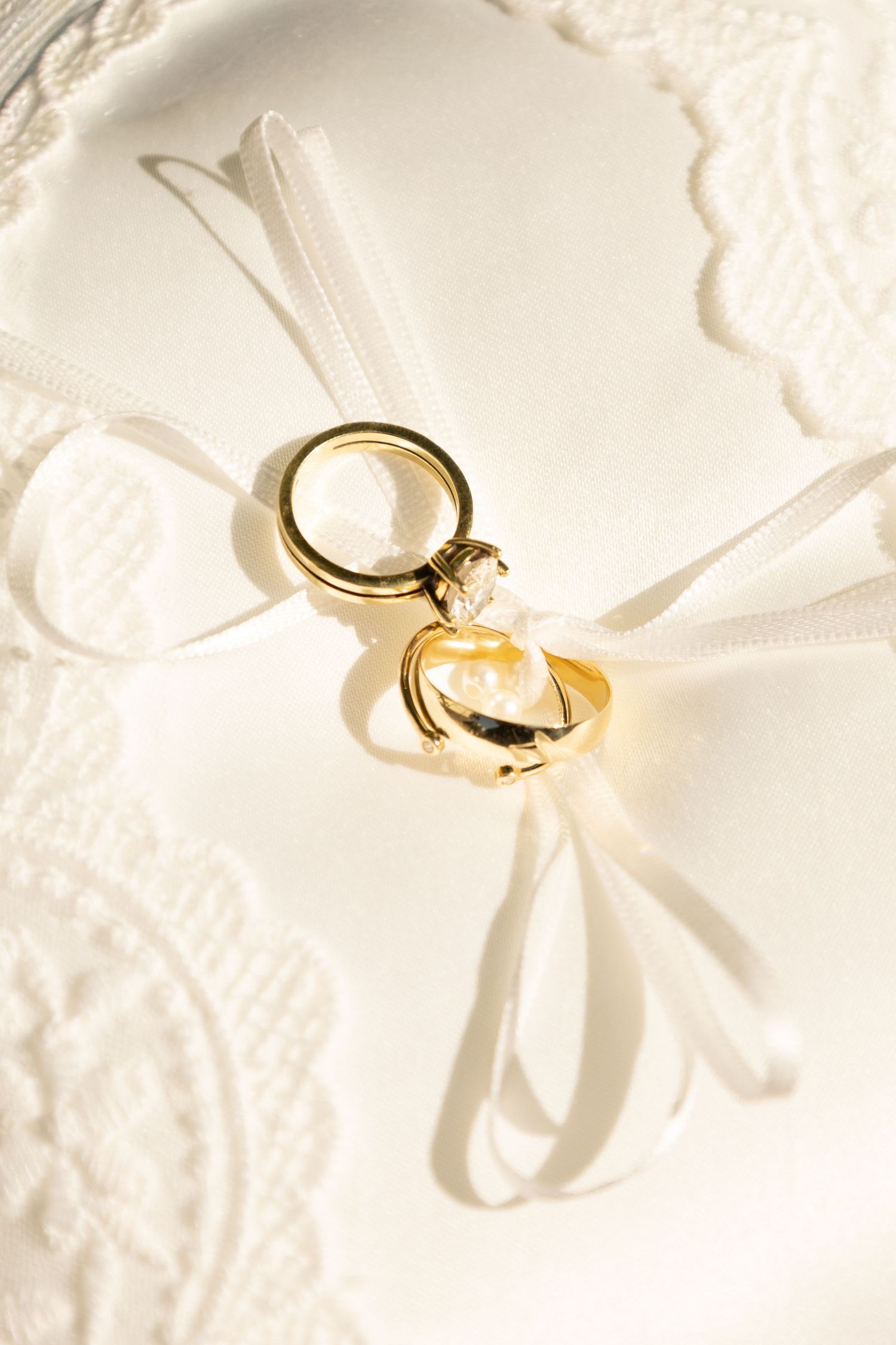 Two gold wedding rings tied with white satin ribbon on an elegant white lace ring bearer pillow.