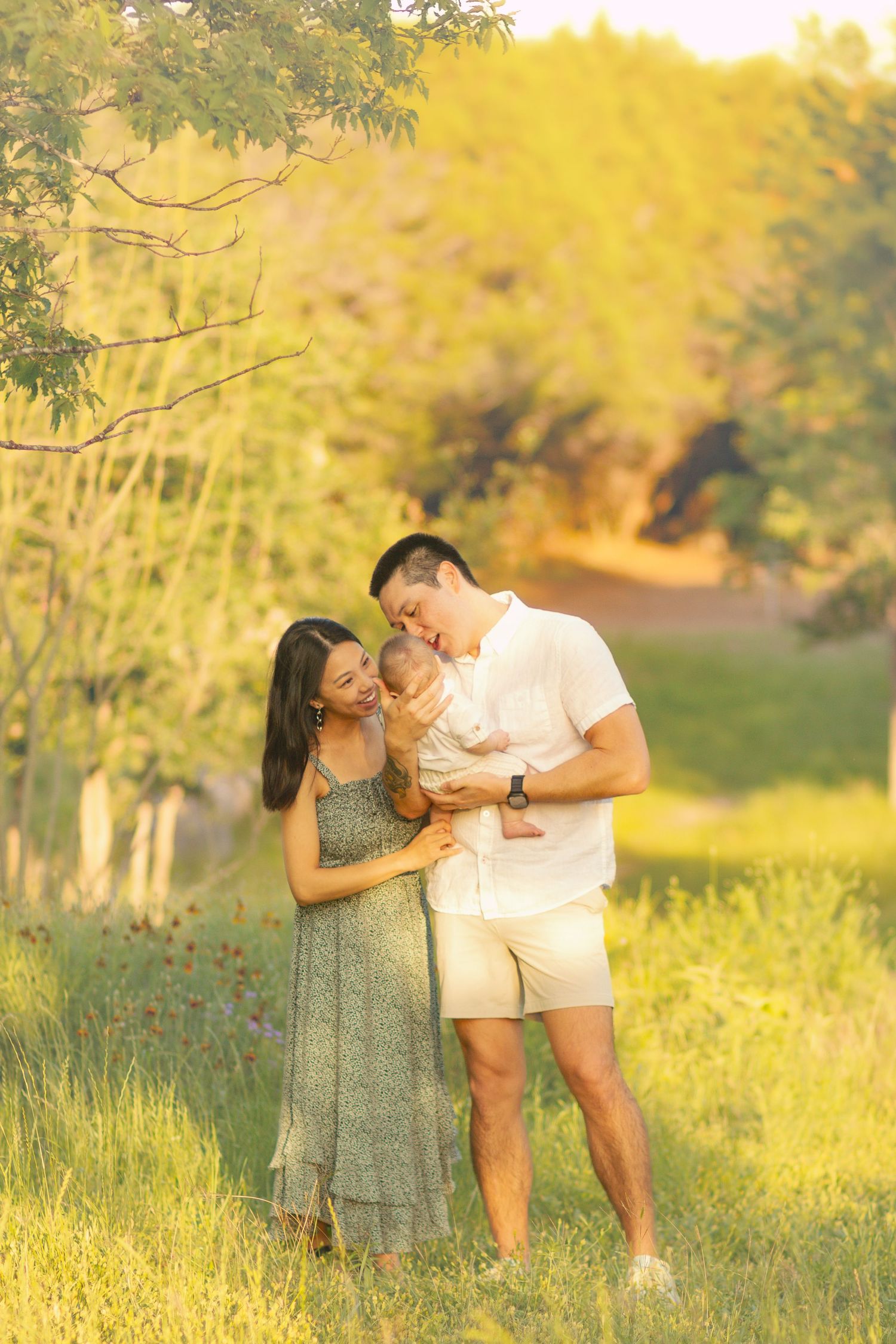 Young Asian family with newborn baby enjoying golden hour outdoors in a lush green meadow.