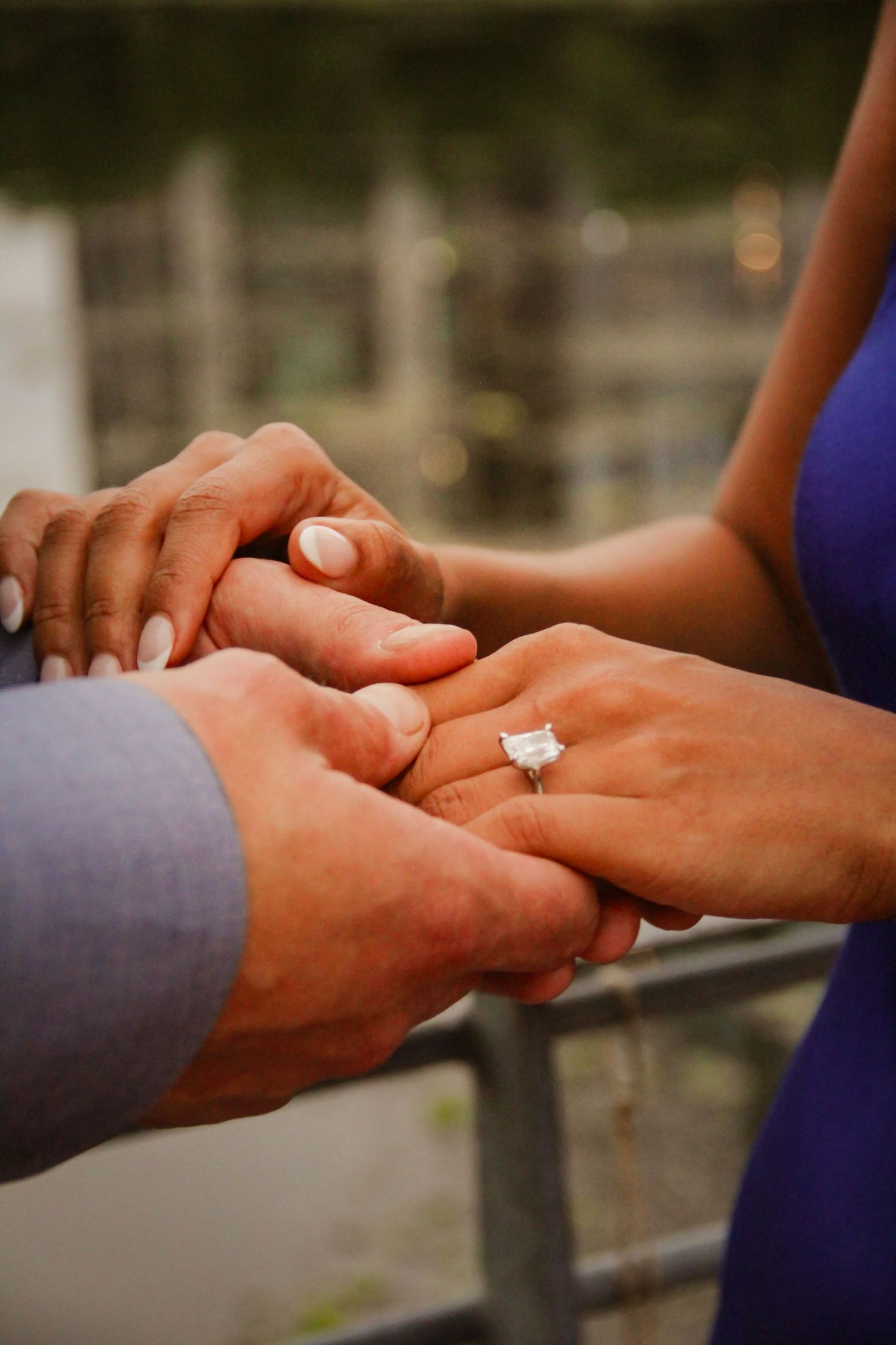 A close-up of a couple holding hands displaying a large emerald-cut diamond engagement ring.