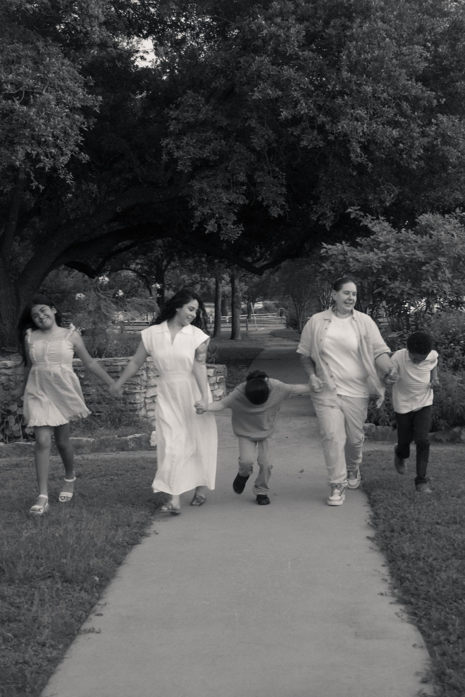 Black and white photo of a family holding hands and walking together on a park path surrounded by trees.