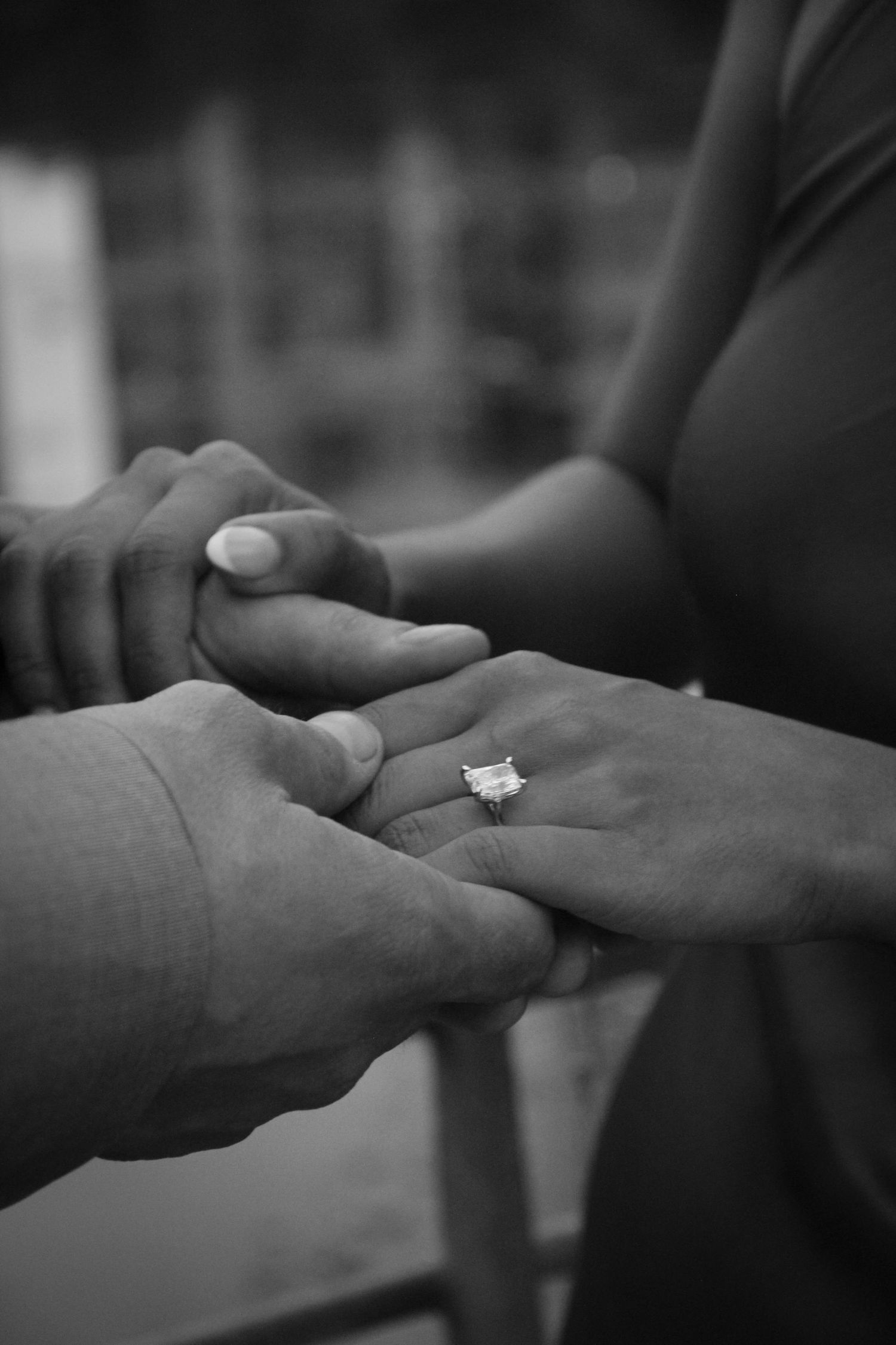 Black and white photo of a couple holding hands with a sparkling diamond engagement ring during a romantic proposal.