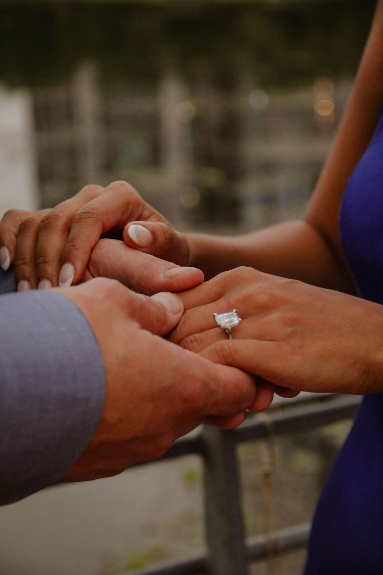 Close-up of a couple holding hands showing off a large emerald cut diamond engagement ring.