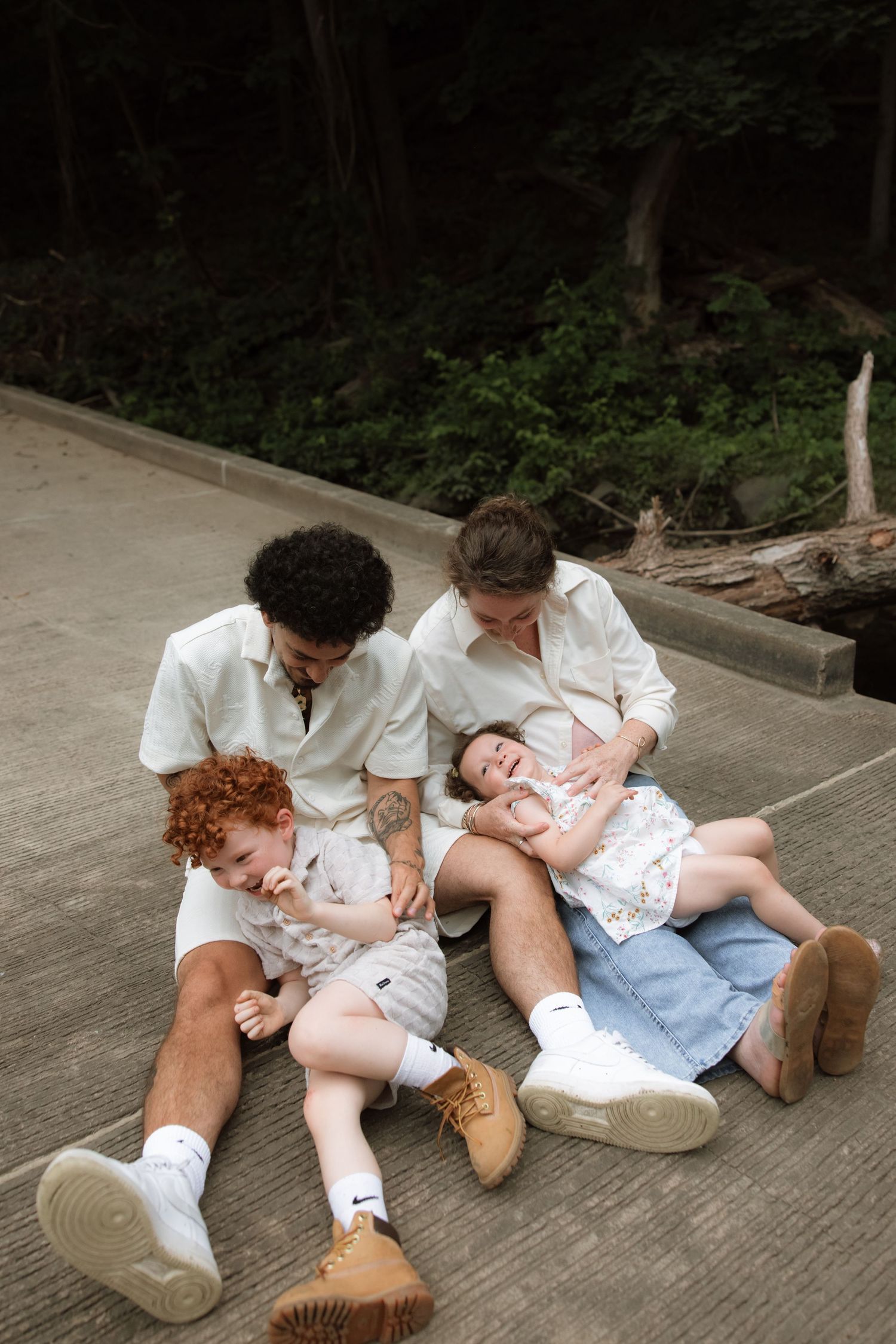 A series of images capturing a family lying down and playing together on a concrete surface in the woods.