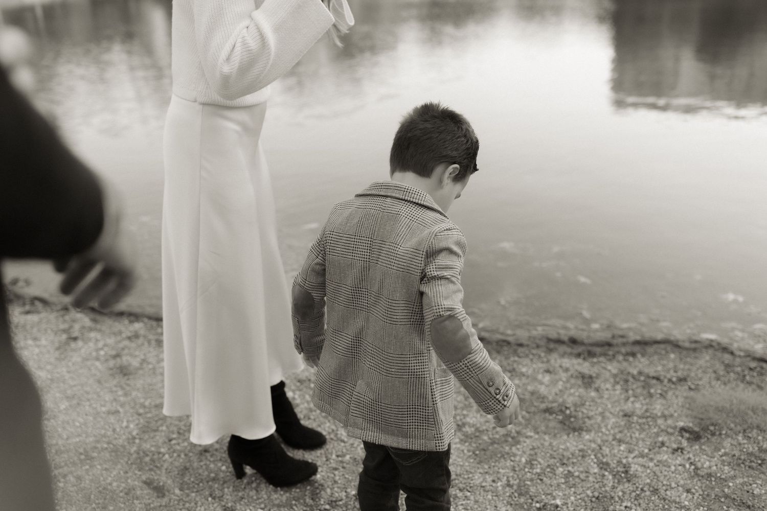 A vintage black and white photograph of someone in white dress standing near a child by a tranquil waterside.