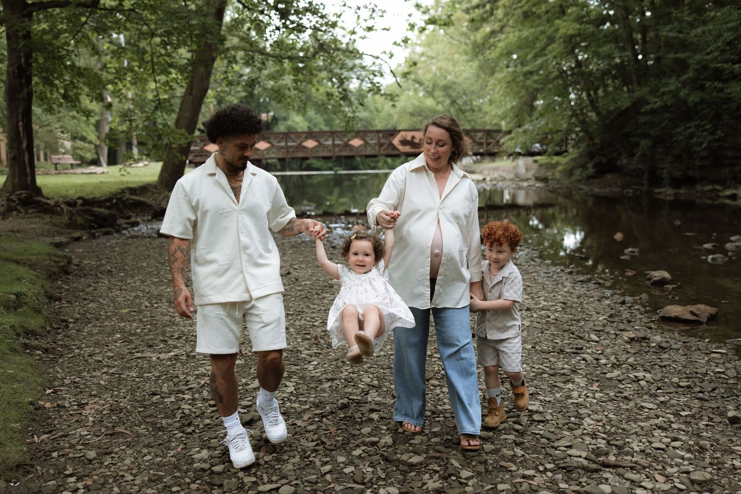 Family members walking together on a leaf-covered trail through a wooded park area.