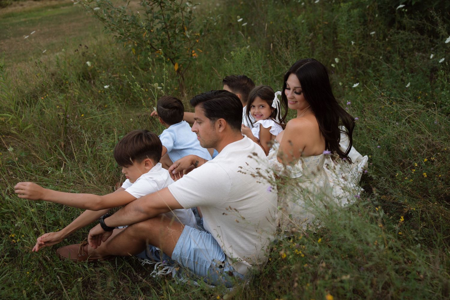 A family sitting together in a grassy meadow during summer wearing white and light blue outfits.