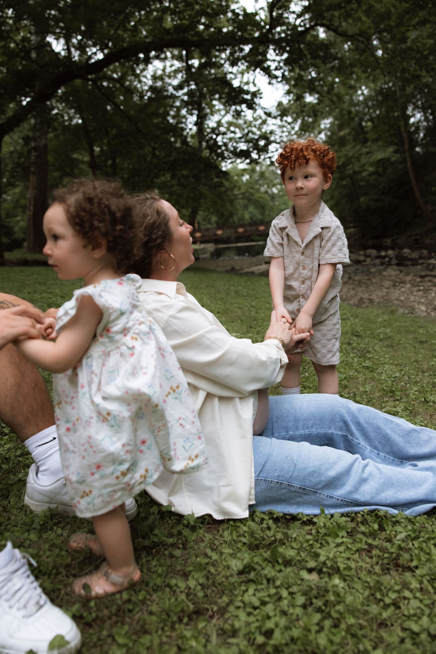 Casual outdoor family playtime on grass with stone wall and trees in background.