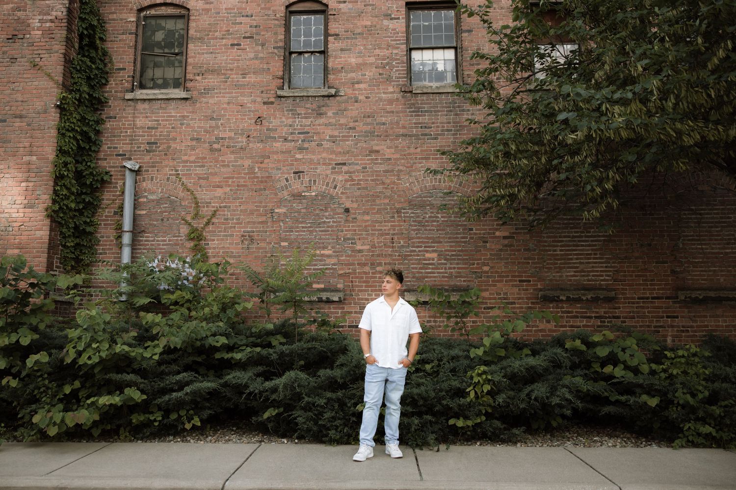 A series of five connected photos showing someone in white clothing walking along a brick wall with greenery.