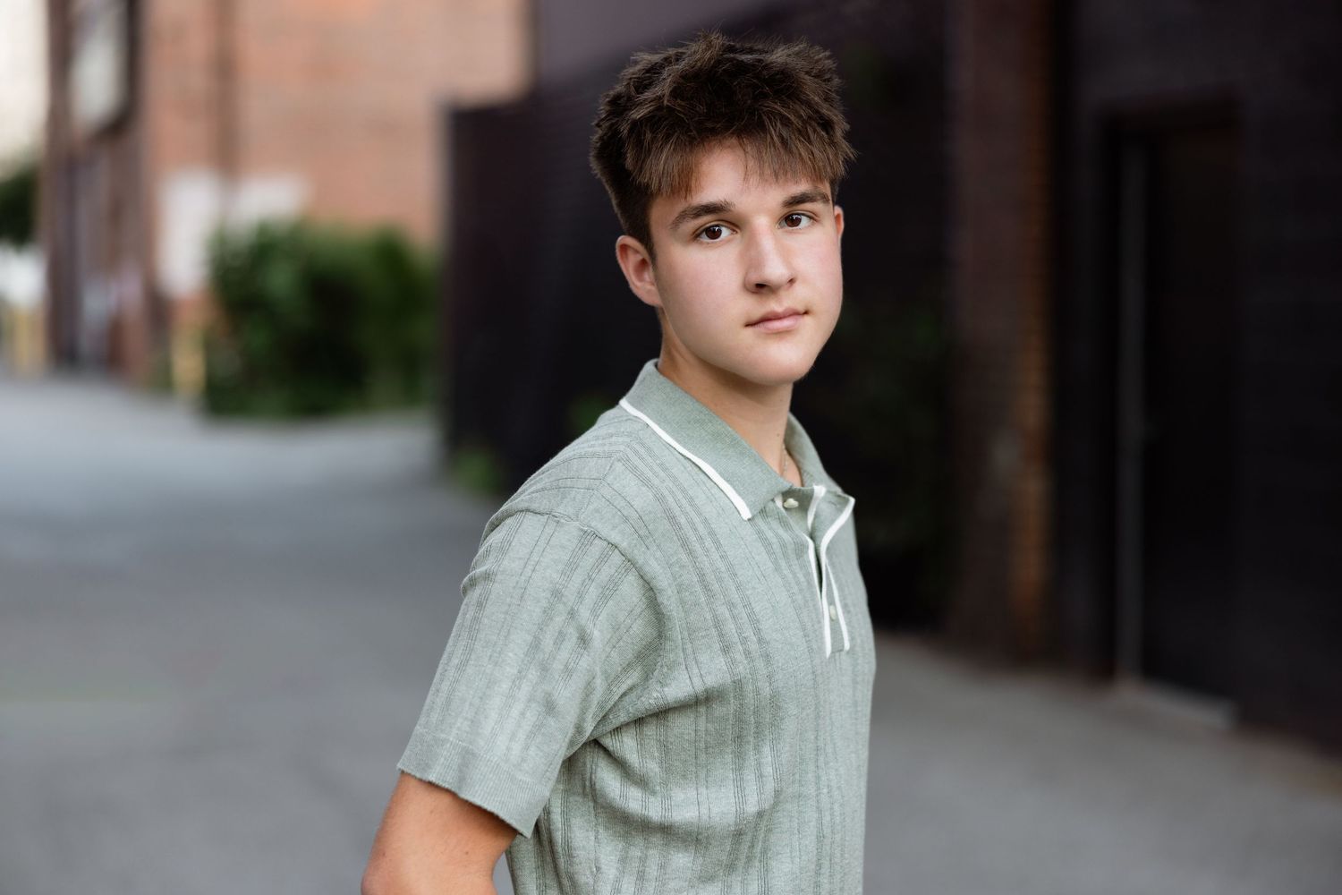 Individual in a light green striped polo shirt poses outdoors against a brick building on a city street.