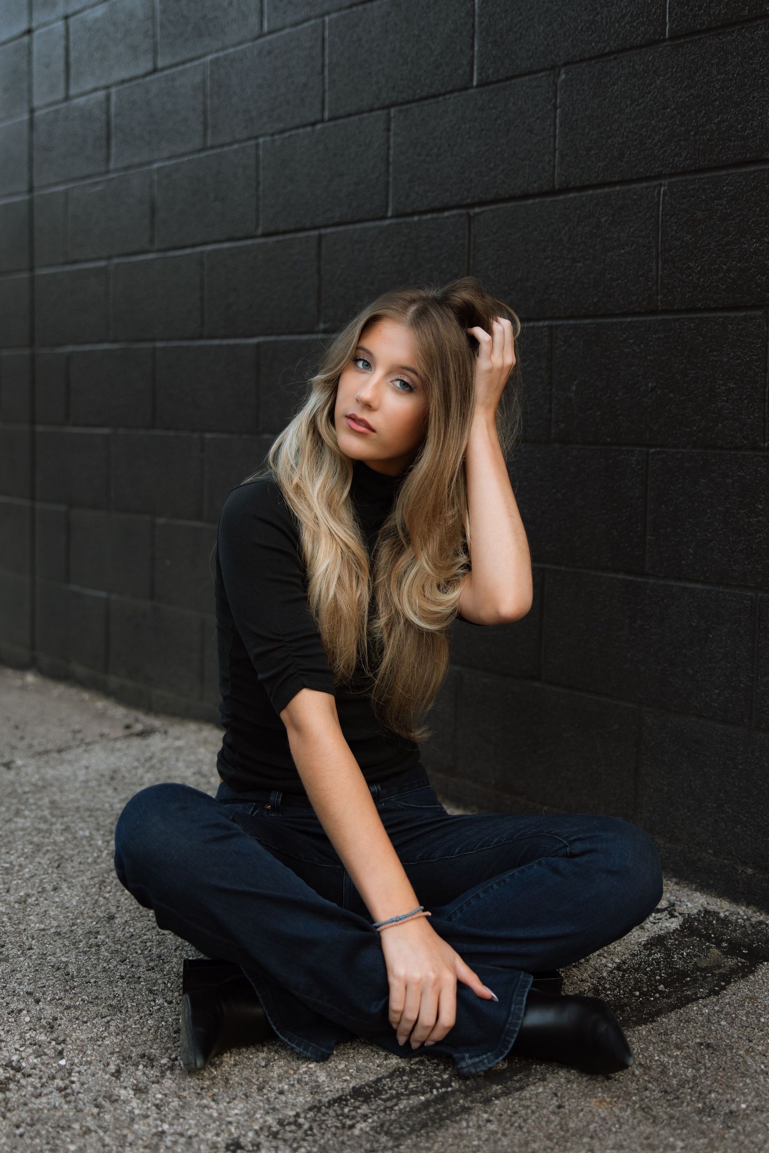 A series of moody portrait shots against a dark wall showing someone sitting on concrete in casual attire.