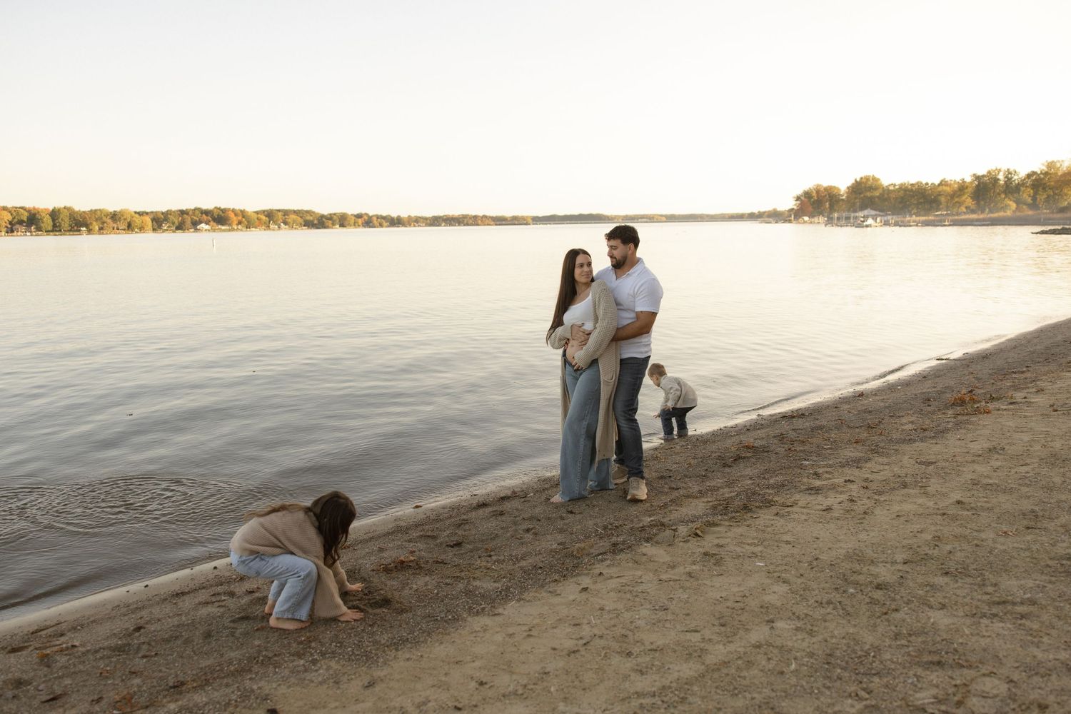 Family enjoying sunset together with dogs on a sandy beach by calm waters.