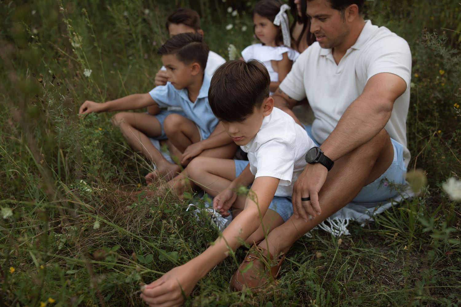 A family in casual attire lounges together on grassy ground during a warm summer day.