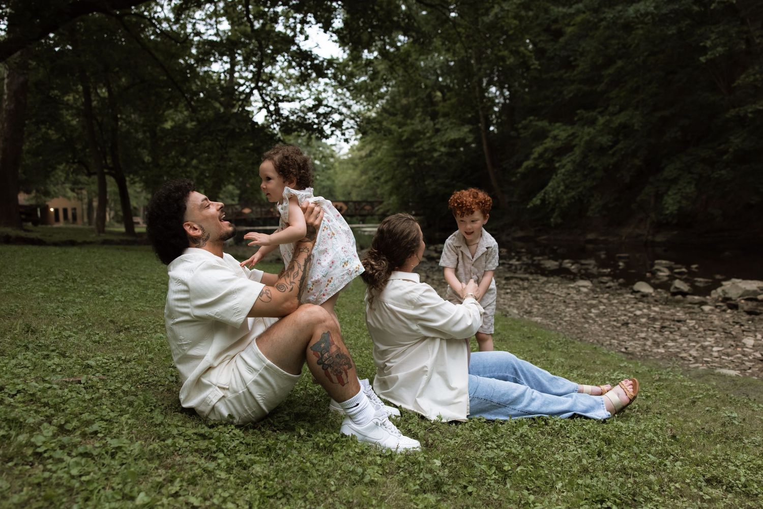 Romantic couple in casual attire relaxes together on a grassy hillside during a warm afternoon outdoors.