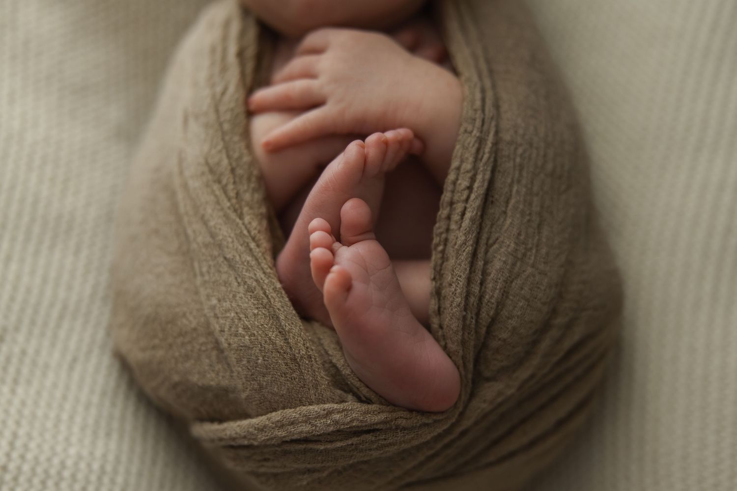 Tiny newborn baby feet wrapped in soft neutral fabric.