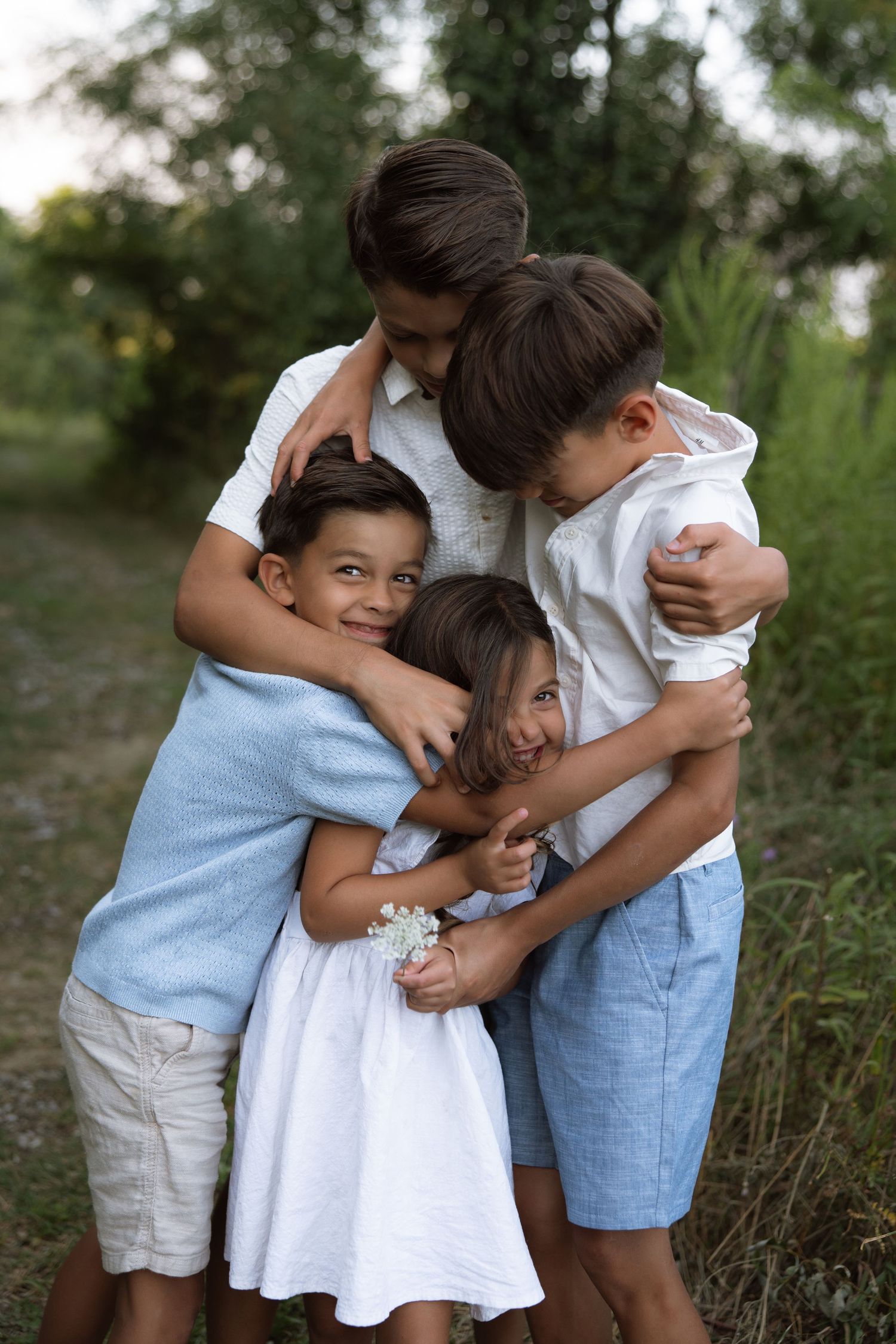 A family wearing white and blue outfits embraces in a tender group hug outdoors during golden hour.