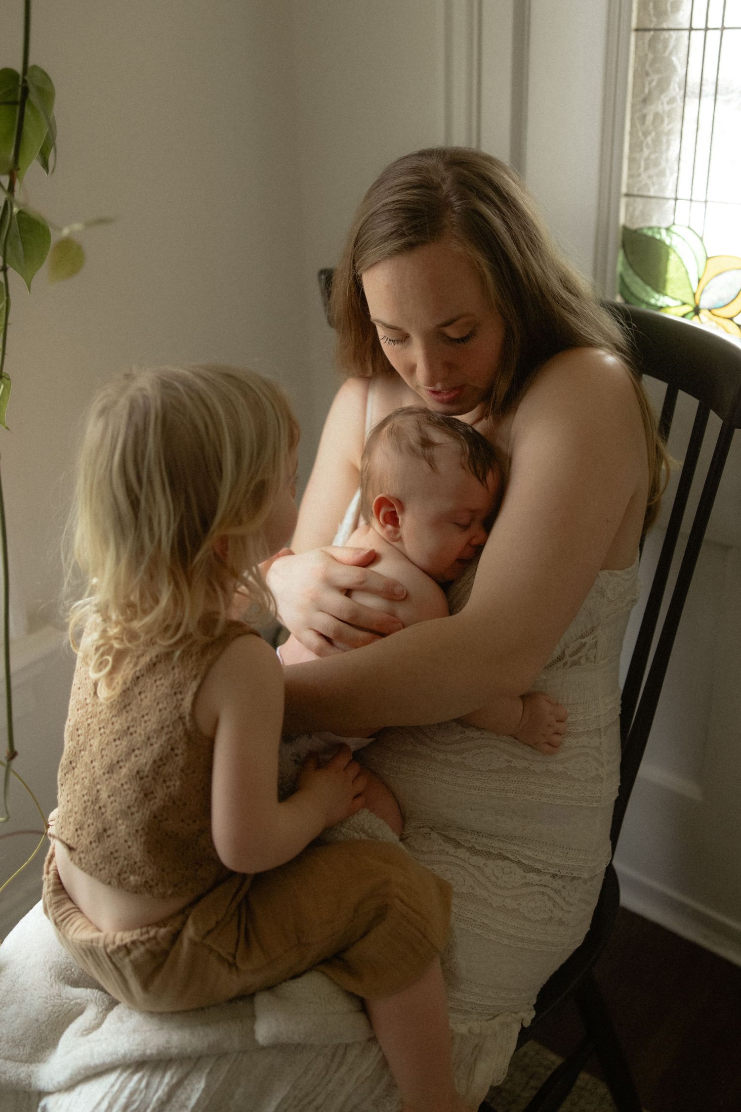A tender moment of a family sitting together near a bright window with houseplants in the background.