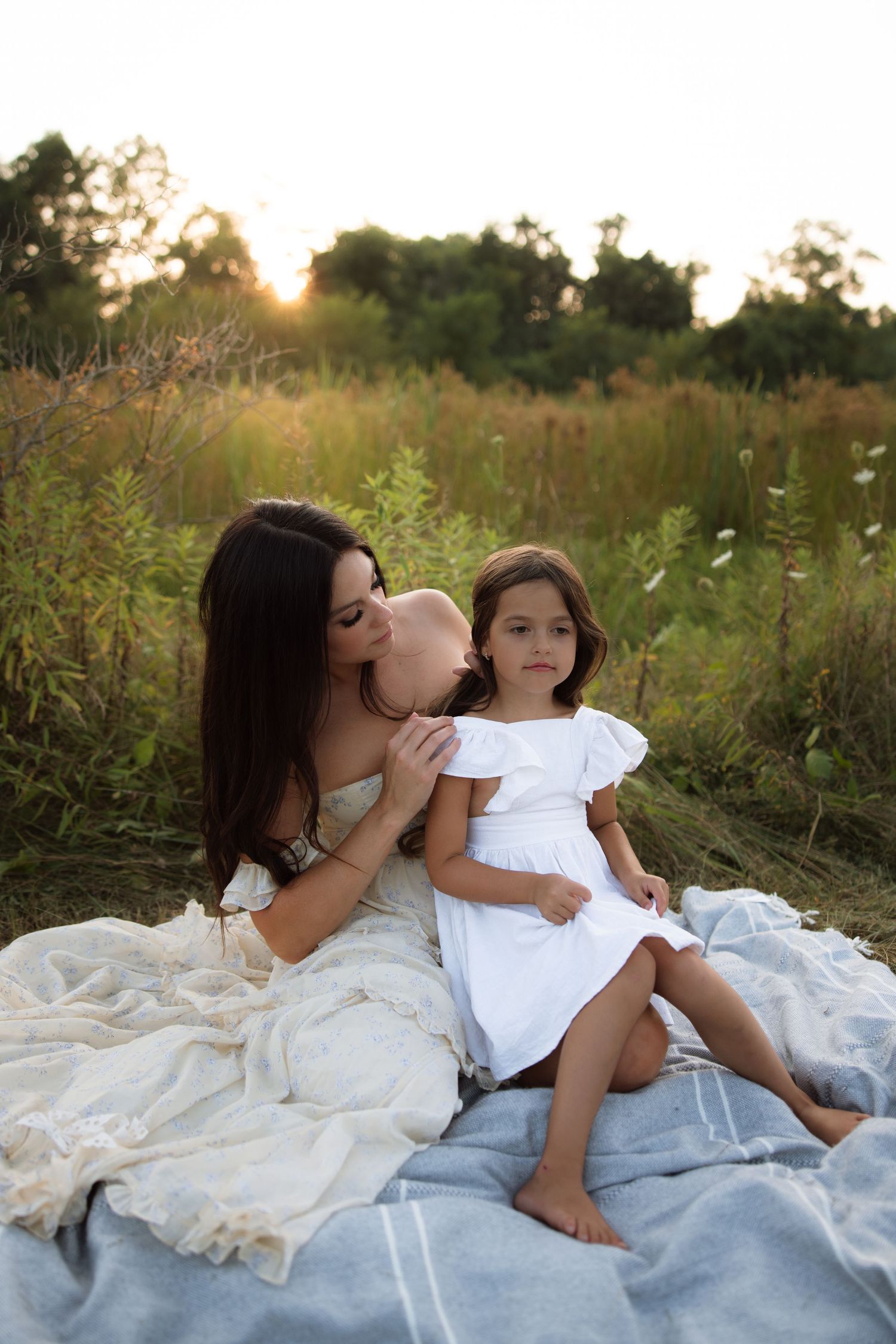 Two people share tender moments together while sitting on a blanket at sunset in a wildflower meadow.
