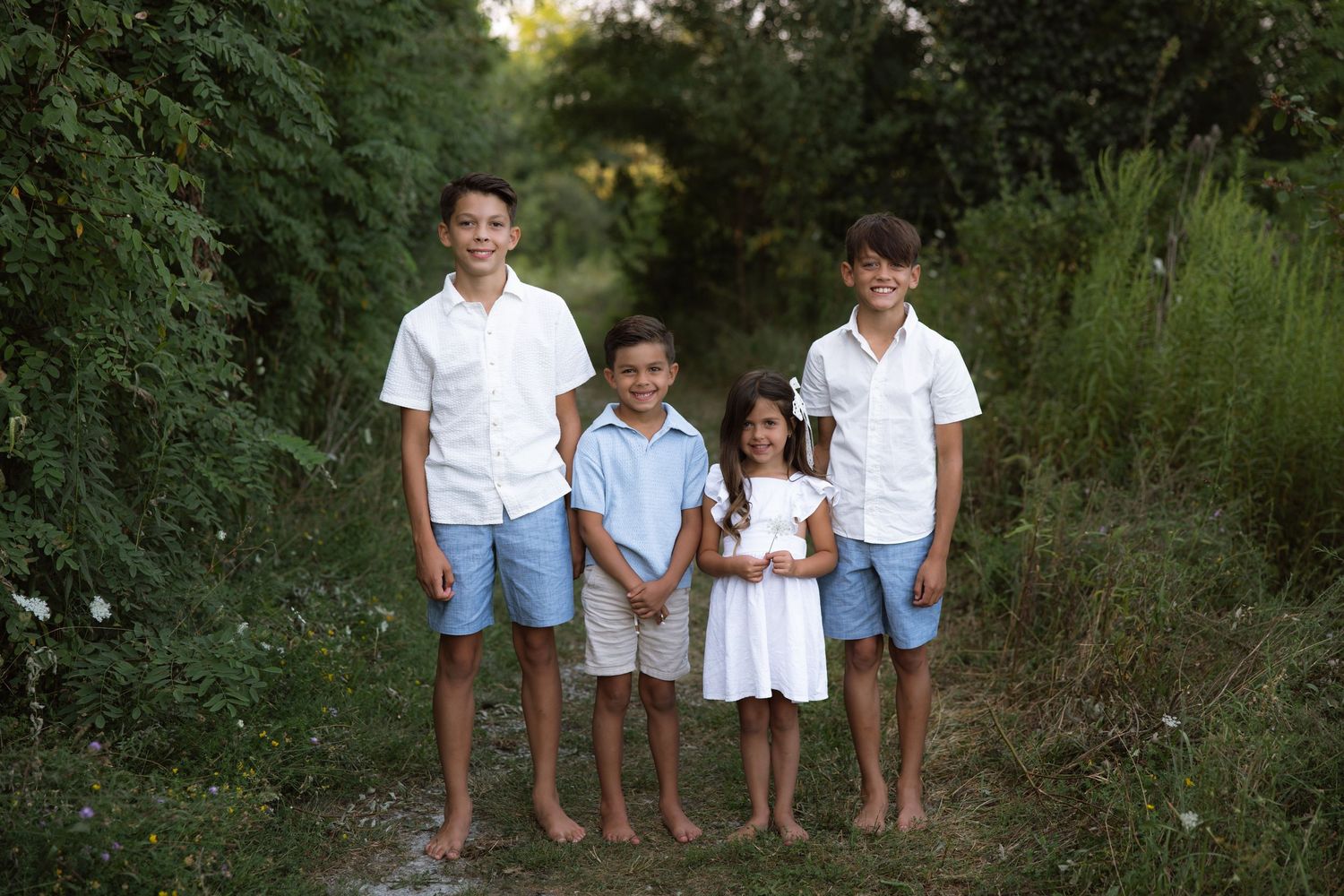 Family wearing coordinated white and blue outfits poses together on a nature path during golden hour.