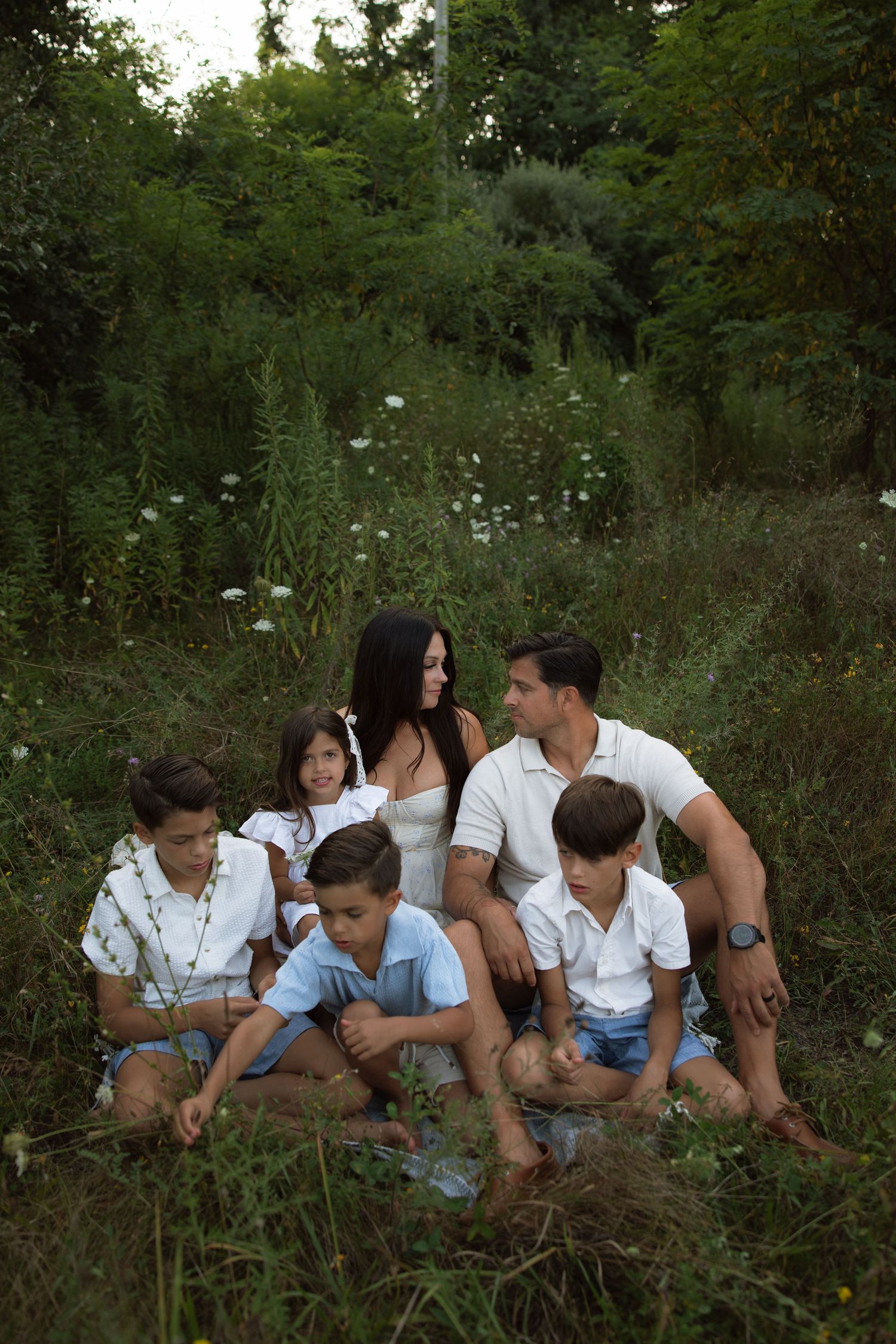 Family members sit together in a grassy field wearing coordinated white and blue summer outfits.