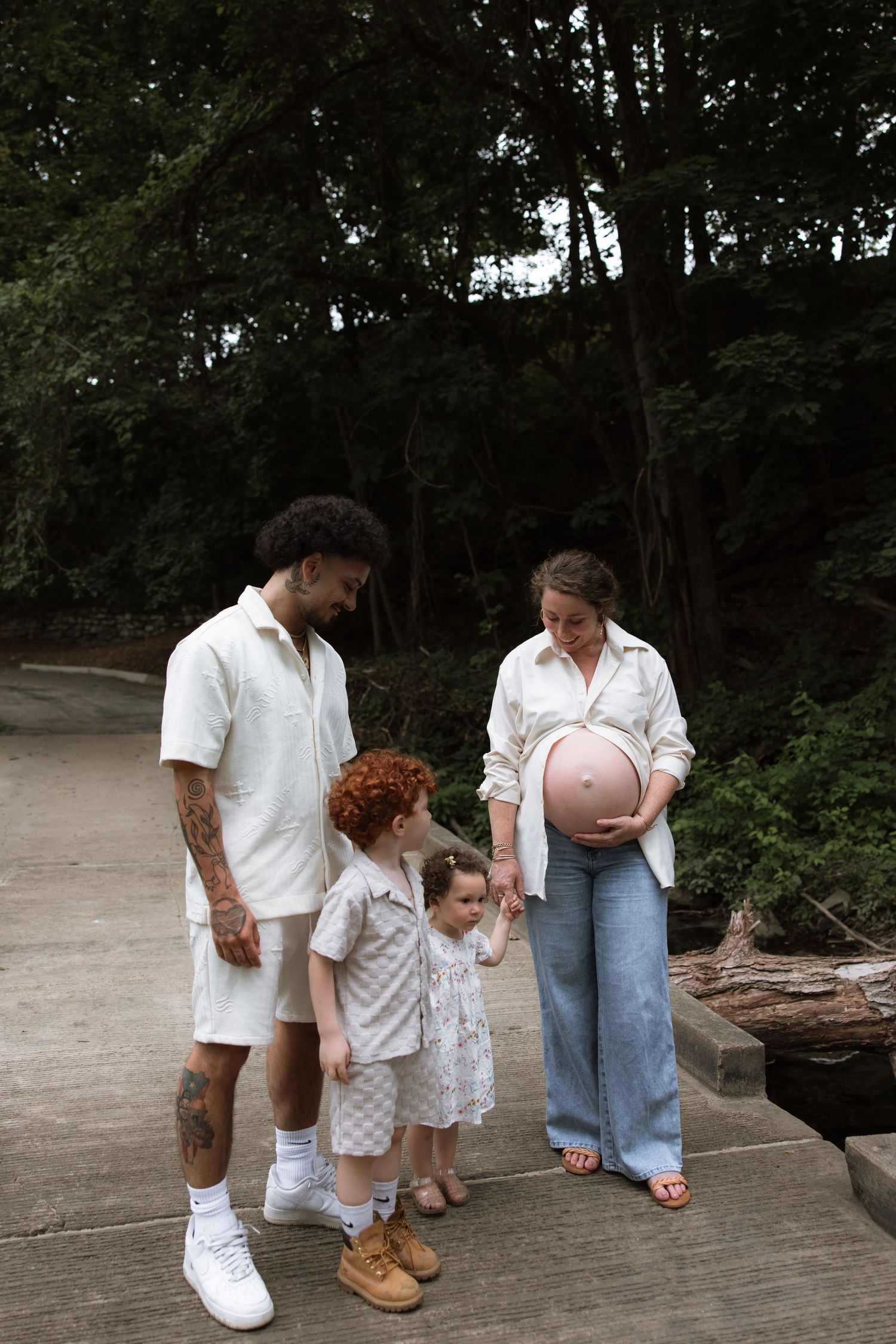 A family in matching white outfits stands together on a wooden deck surrounded by trees in a park setting.