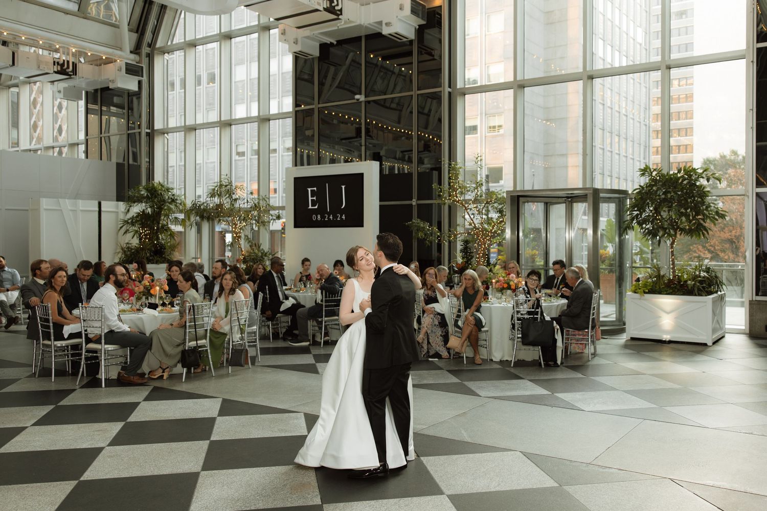 A first dance at a modern wedding reception in a sleek venue with checkerboard floors and large windows.
