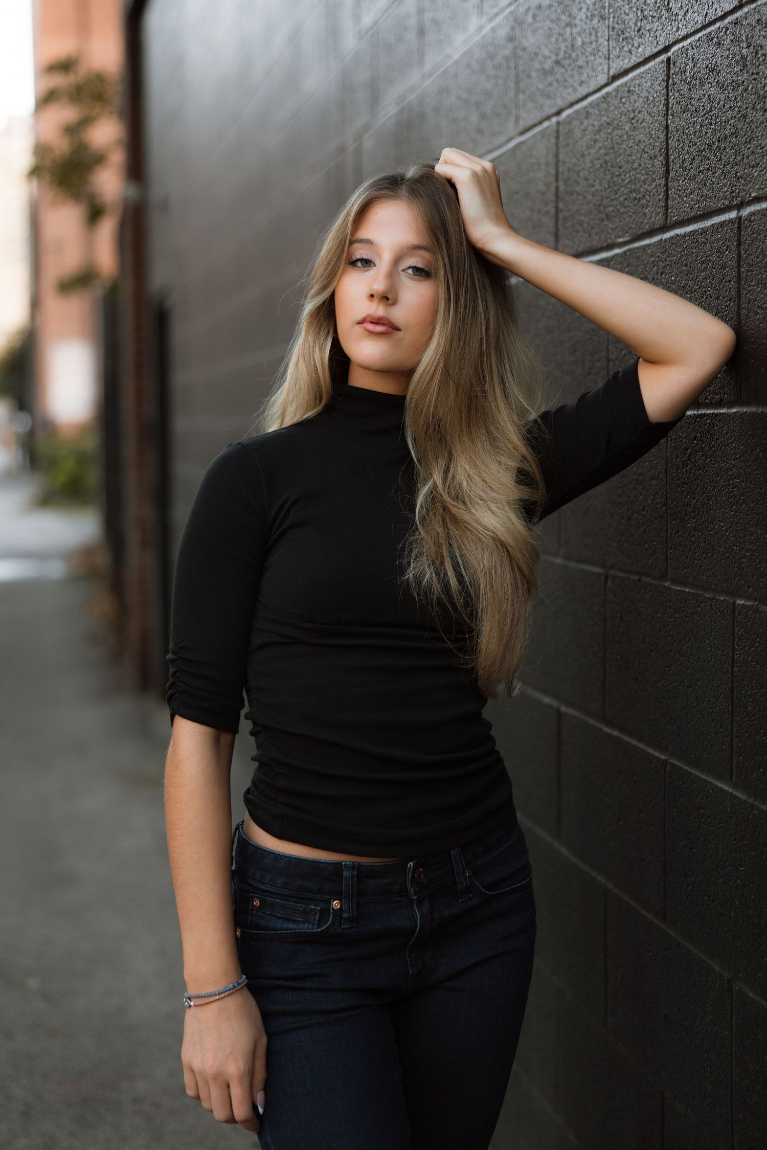 A series of five fashion portraits showing a person in a black top and jeans posing against a dark textured wall.