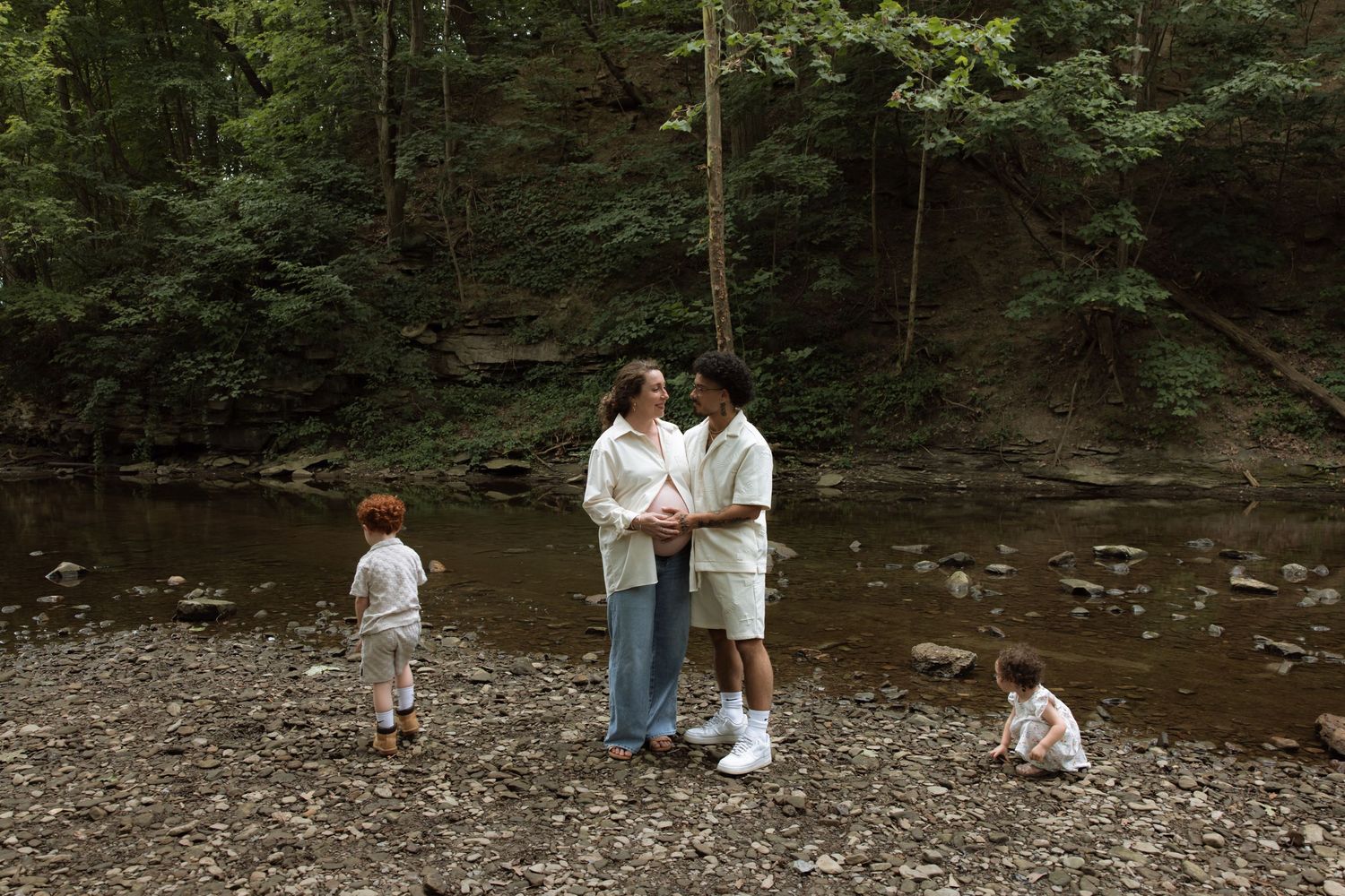 People enjoying a summer day exploring and splashing in a shallow creek surrounded by lush forest trees.