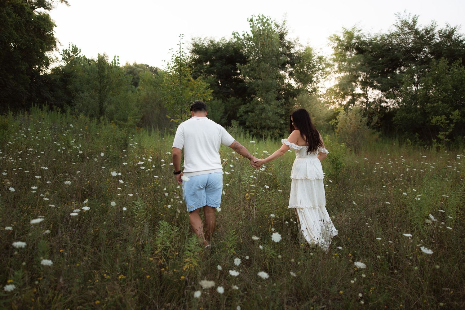 A couple walks hand in hand through a blooming wildflower meadow on a summer evening.