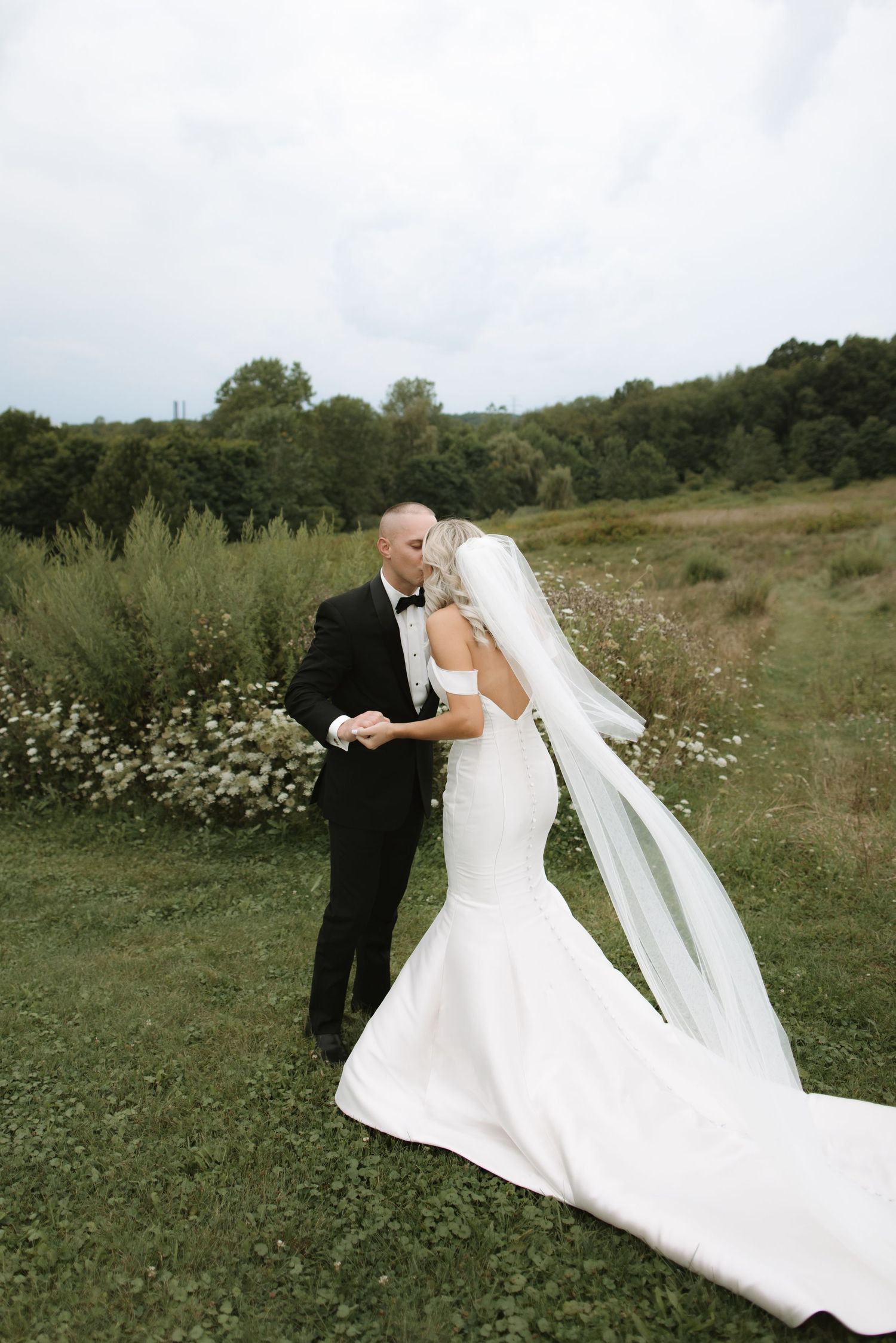 Romantic wedding photography in a lush meadow with wildflowers and a flowing white mermaid gown with long veil.