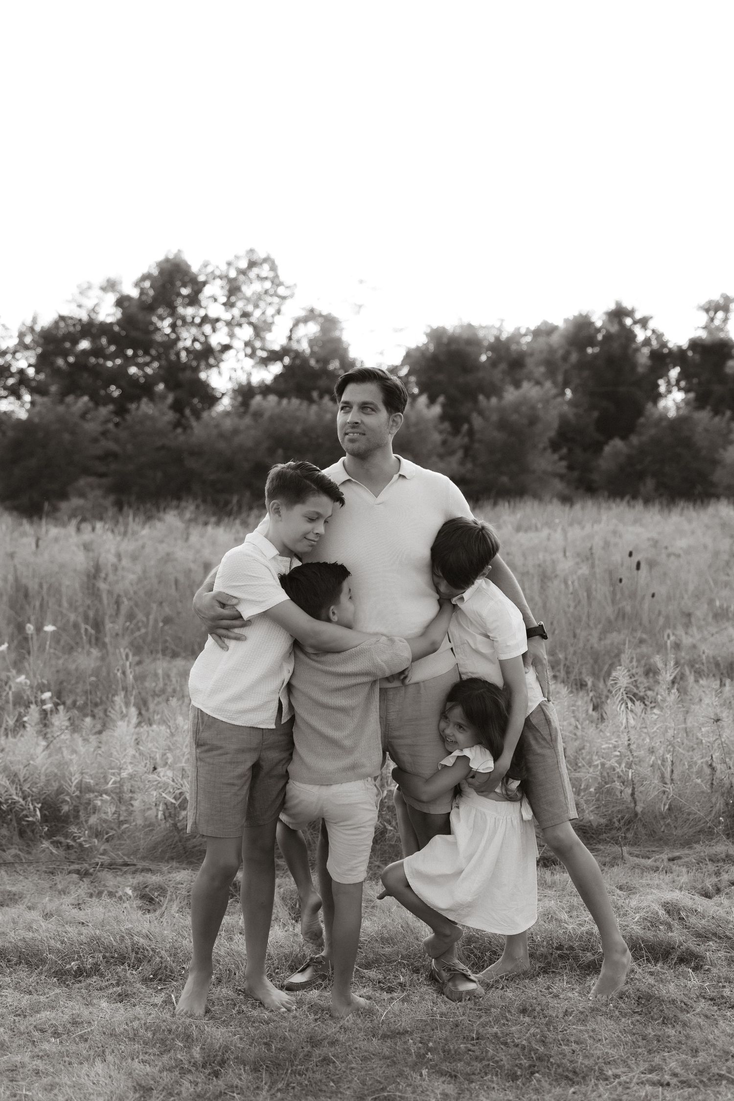 A family shares joyful moments together in a sunlit meadow with tall grass in a series of black and white photos.
