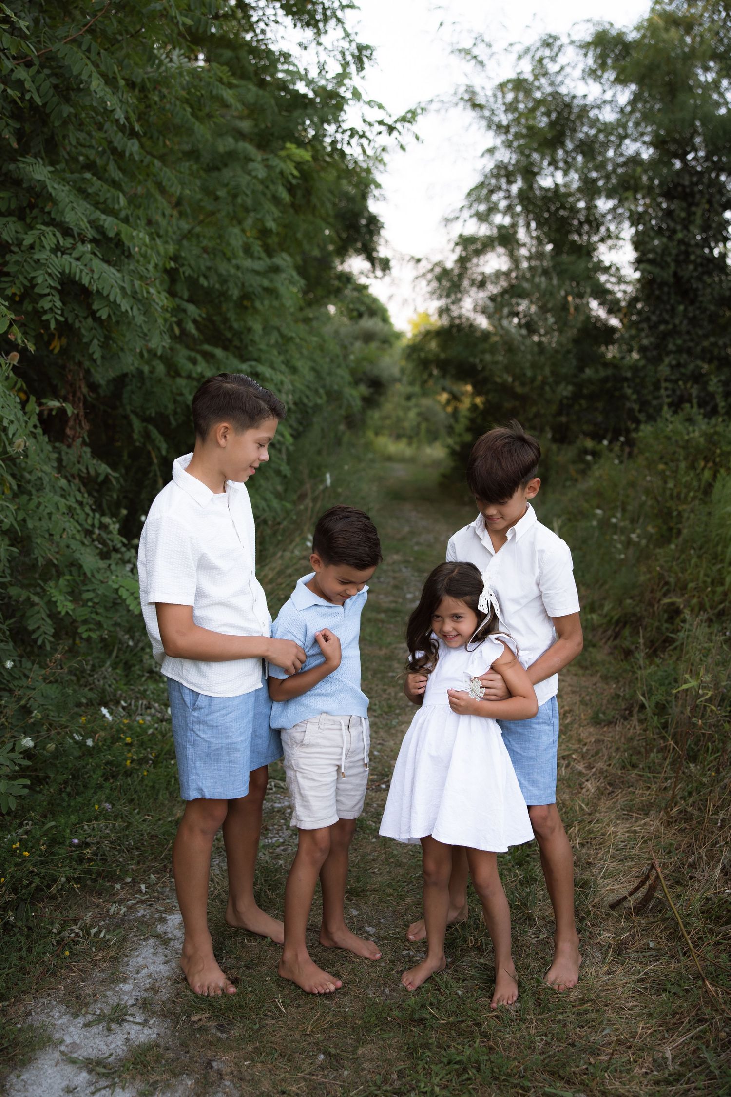 A sequence of candid moments between siblings in white and blue outfits playing outdoors together.