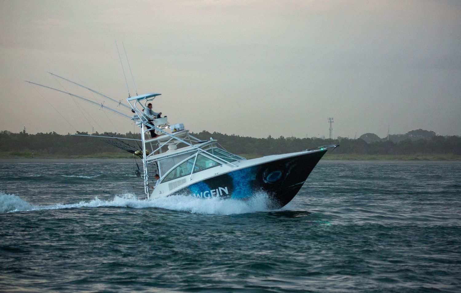 White sport fishing vessel cuts through rough seas with dramatic wave spray.