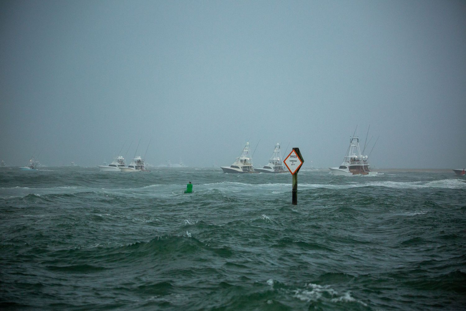 Multiple fishing vessels battle rough seas with white caps and choppy water.