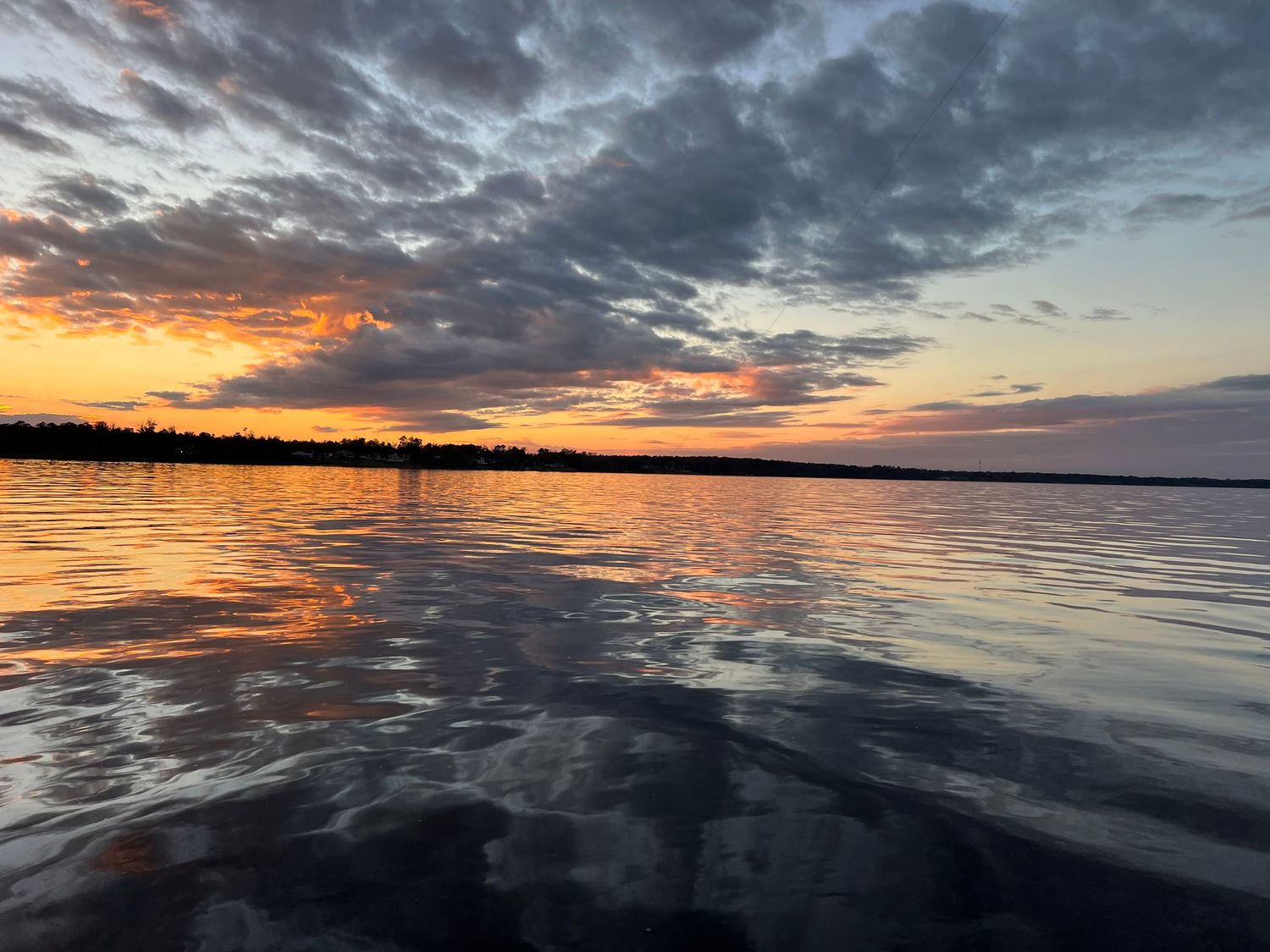 Panoramic sunset over a calm lake with dramatic clouds reflecting on the rippled water surface.