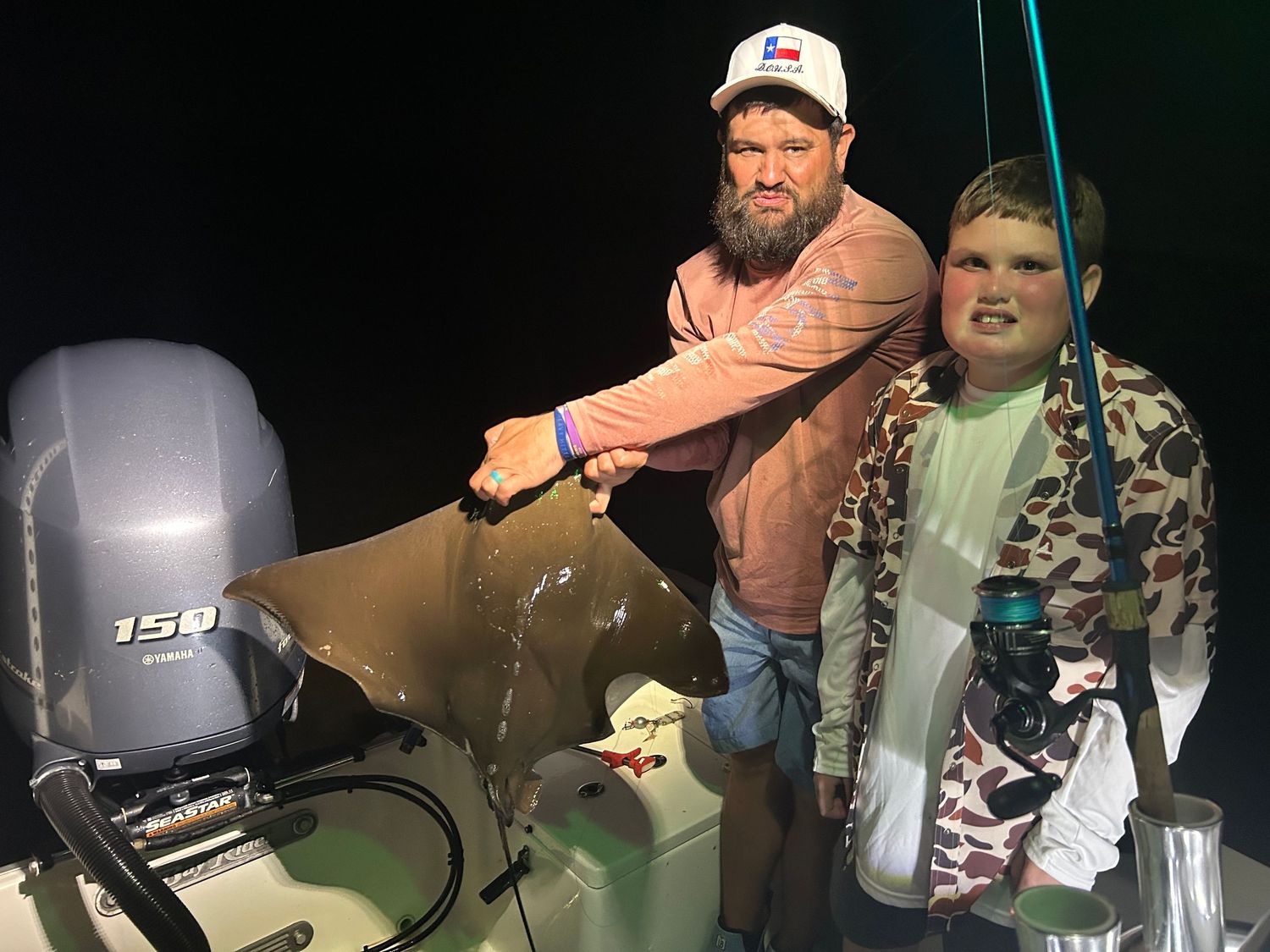Fishermen aboard boat at night preparing equipment near outboard motor.