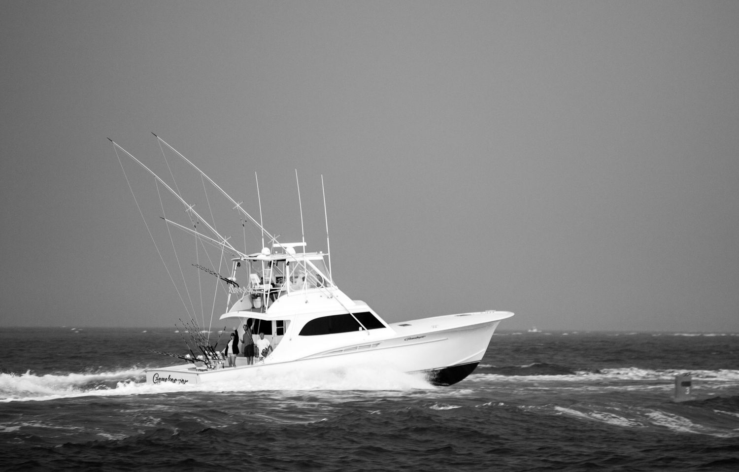 Black and white image of sport fishing vessel navigating through rough ocean waves.