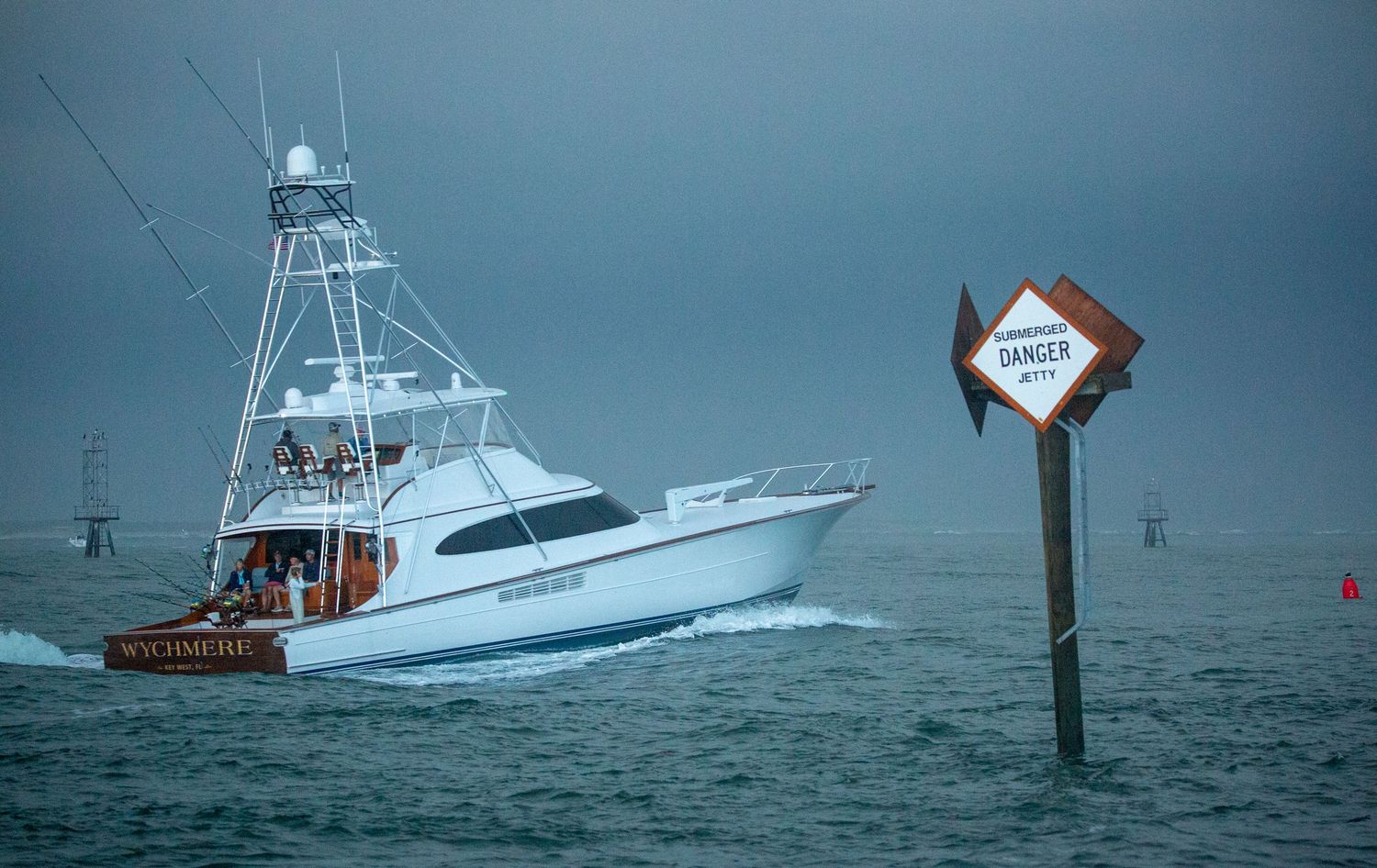 Large sport fishing boat navigating through rough seas during a storm near a channel marker.