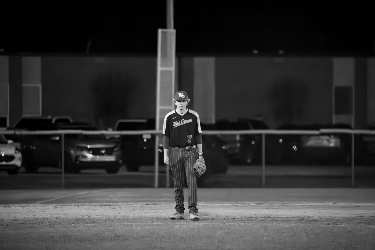 Baseball player standing alone on field at night under lights.
