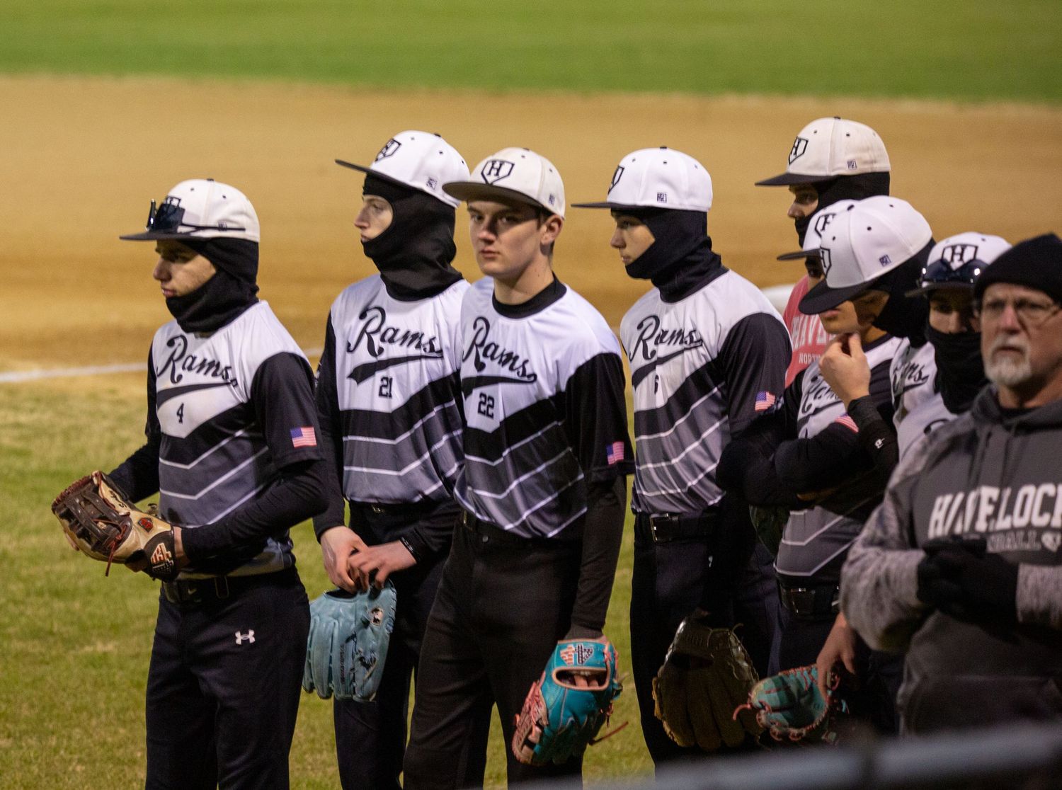 Baseball team lined up along dugout fence wearing matching white and grey uniforms.