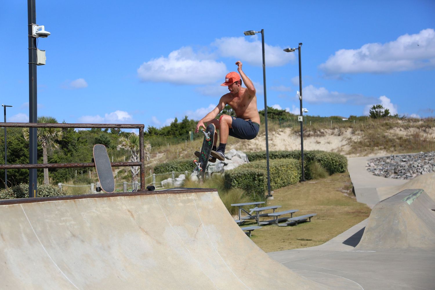 A series of skateboarders performing tricks on a concrete skate park with blue sky and coastal terrain in the background.