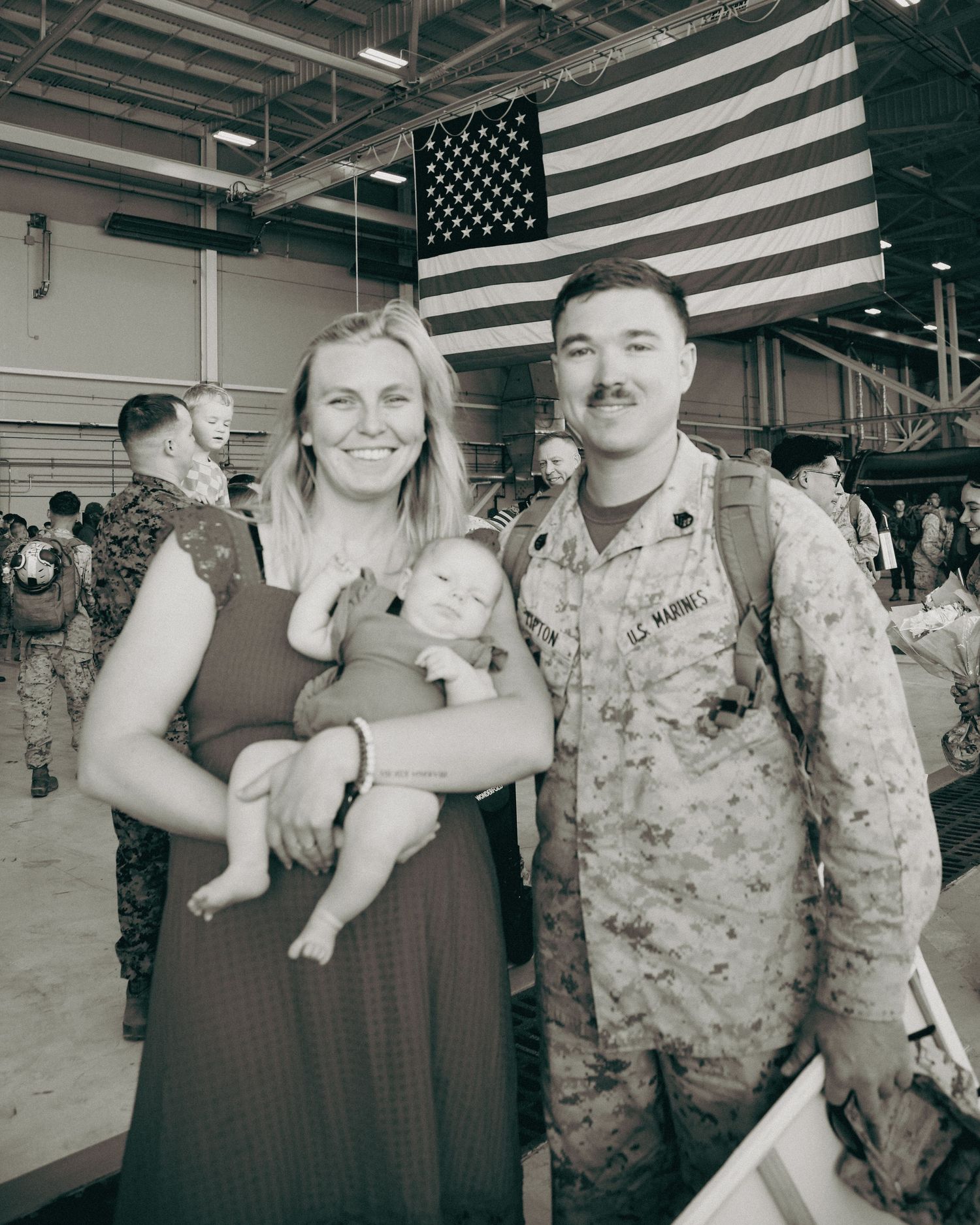 Military homecoming ceremony with American flag displayed prominently in an indoor facility.